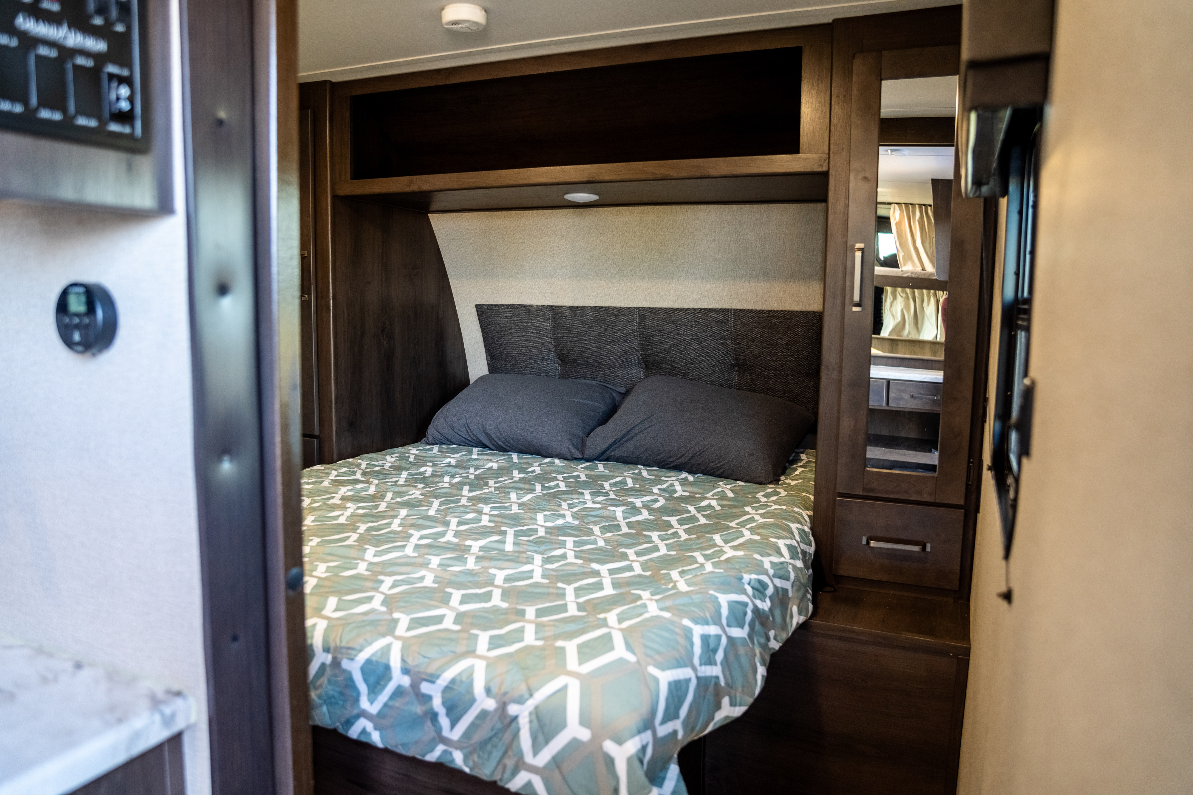 Cozy RV rental bedroom showing a bed, headboard, overhead storage, and mirrored wardrobe for your trip.. Grand Design Transcend Xplor 2023