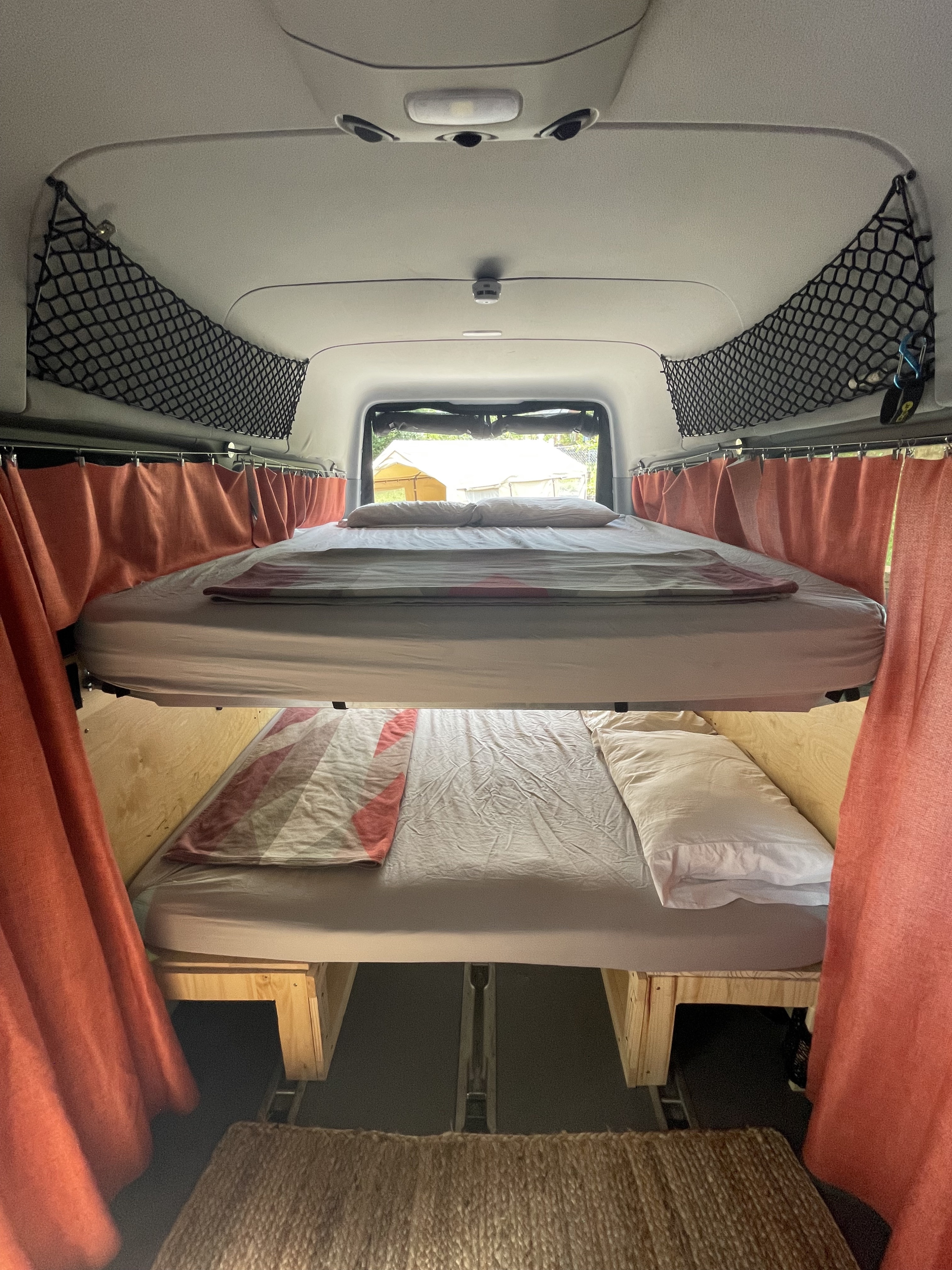 Bunk beds inside an RV rental with practical storage nets and curtains, ideal for cozy camping adventures.. Mercedes Sprinter 2015