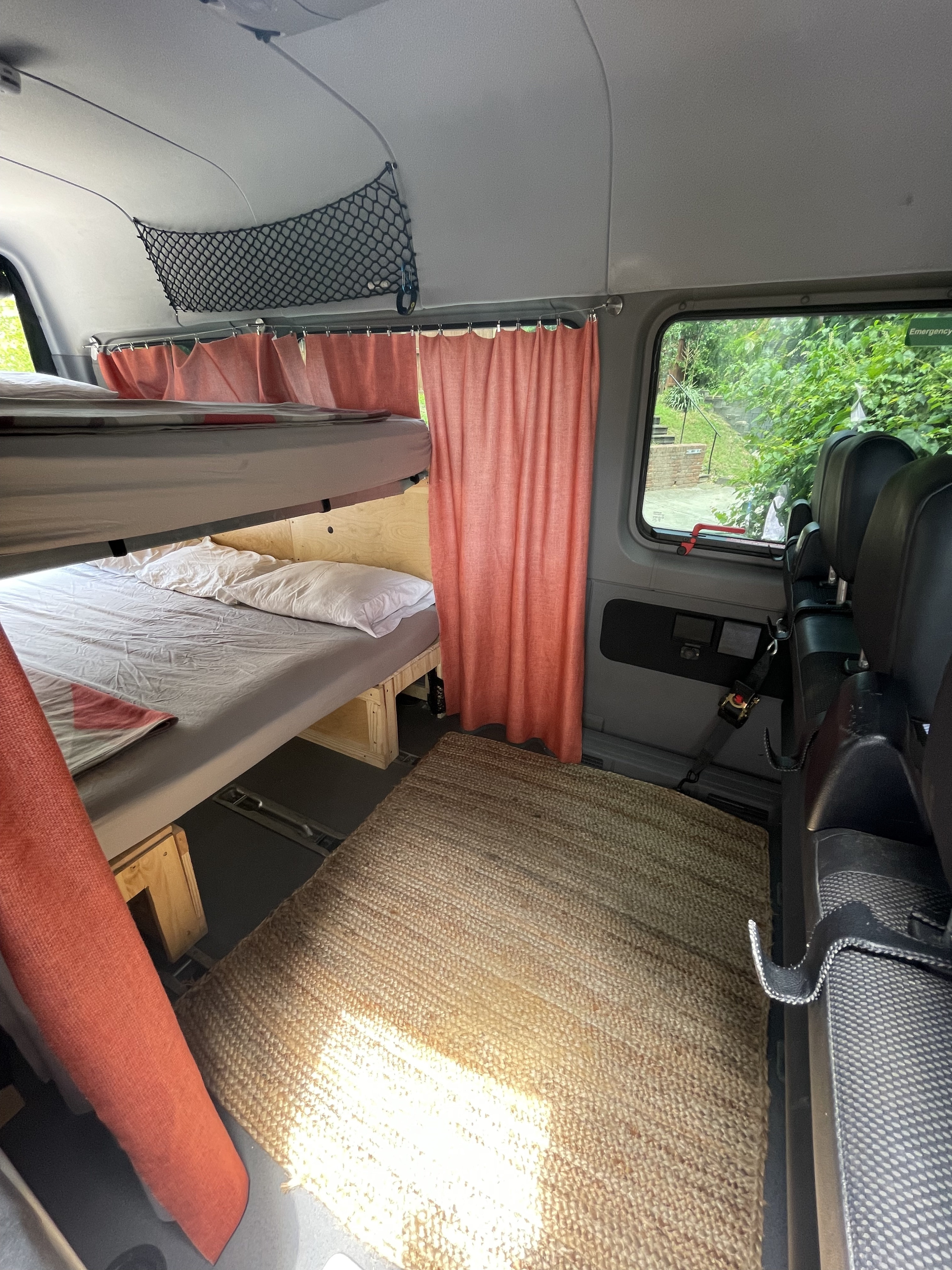 RV rental interior featuring bunk beds with white bedding, privacy curtains, and a woven floor rug, maximizing compact space.. Mercedes Sprinter 2015