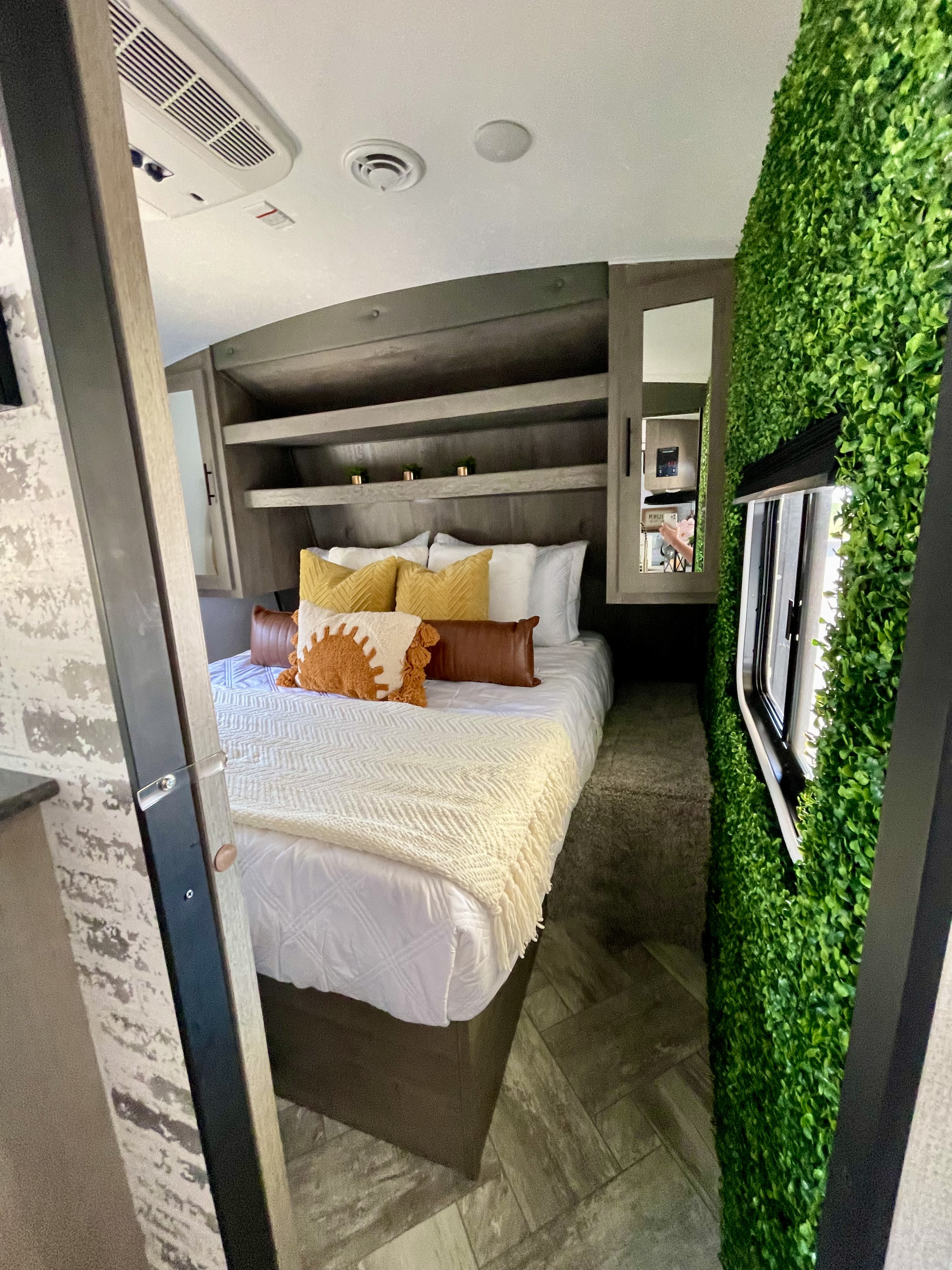 Modern RV rental bedroom featuring a cozy bed, built-in storage, and a unique green foliage accent wall with a window.. Keystone RV Springdale 2021
