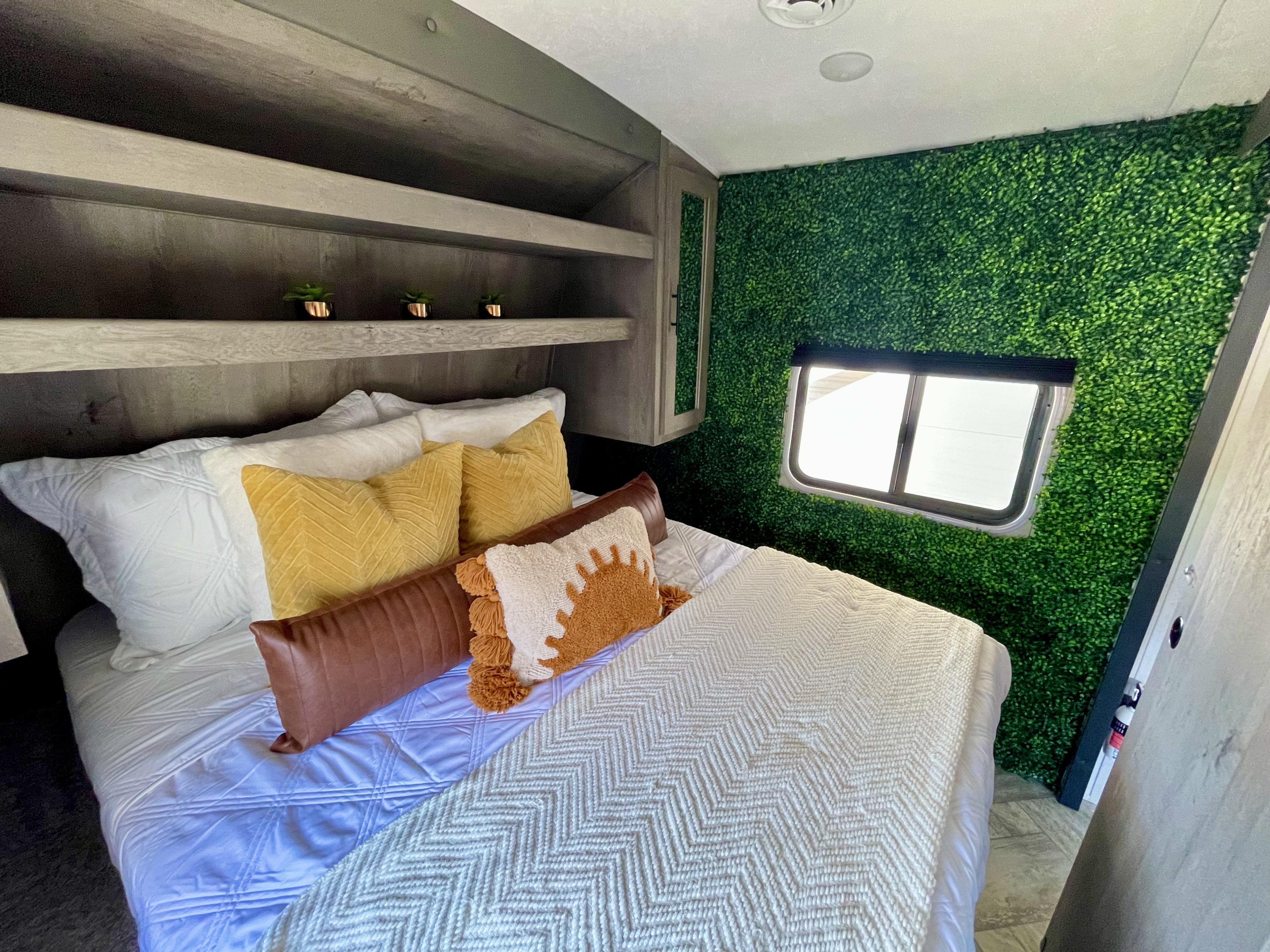 Cozy RV rental bedroom with a faux hedge wall, comfy bed, and built-in shelves.. Keystone RV Springdale 2021