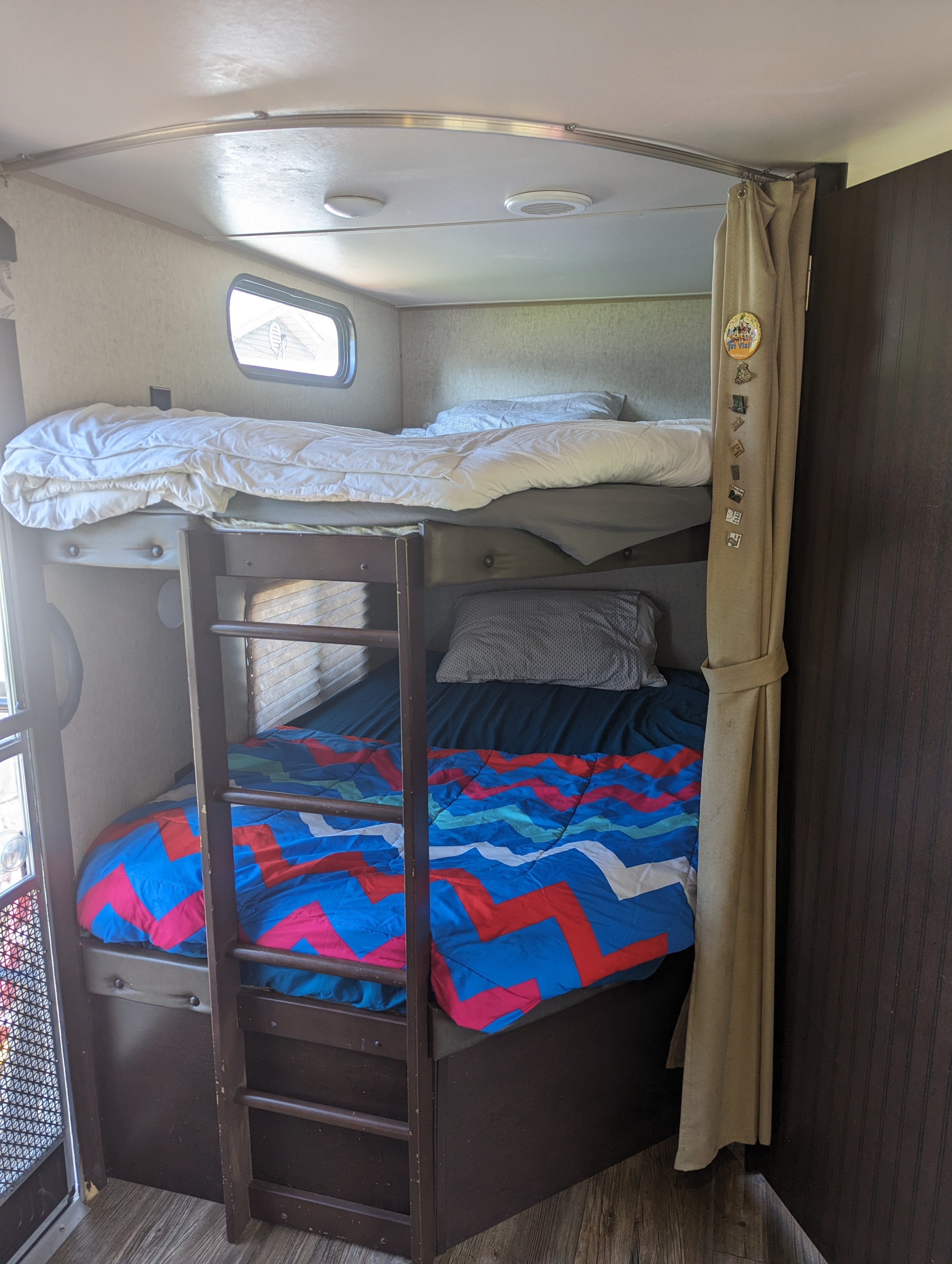 Cozy bunk beds in an RV rental, featuring a white top bunk and vibrant blue/red zigzag comforter on the bottom.. Forest River Cherokee 2016