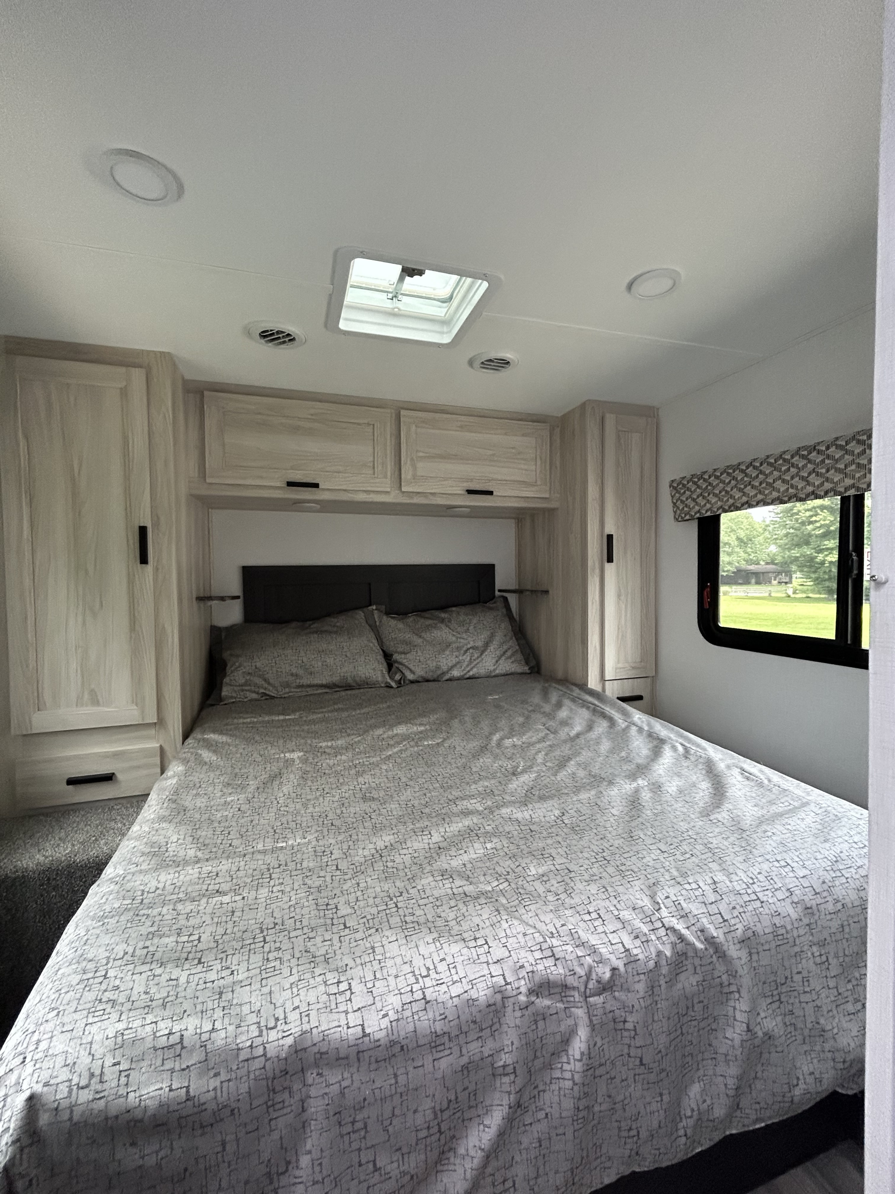 Experience comfort in this RV rental bedroom, featuring a spacious bed, ample storage, and natural light from the window and skylight.. Forest River Other 2023