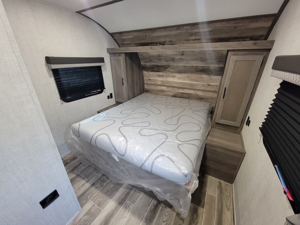 Clean, modern RV rental bedroom featuring a new bed, built-in storage, wood-look accents, and side windows.. Gulf Stream Amerilite 22RSD 2022