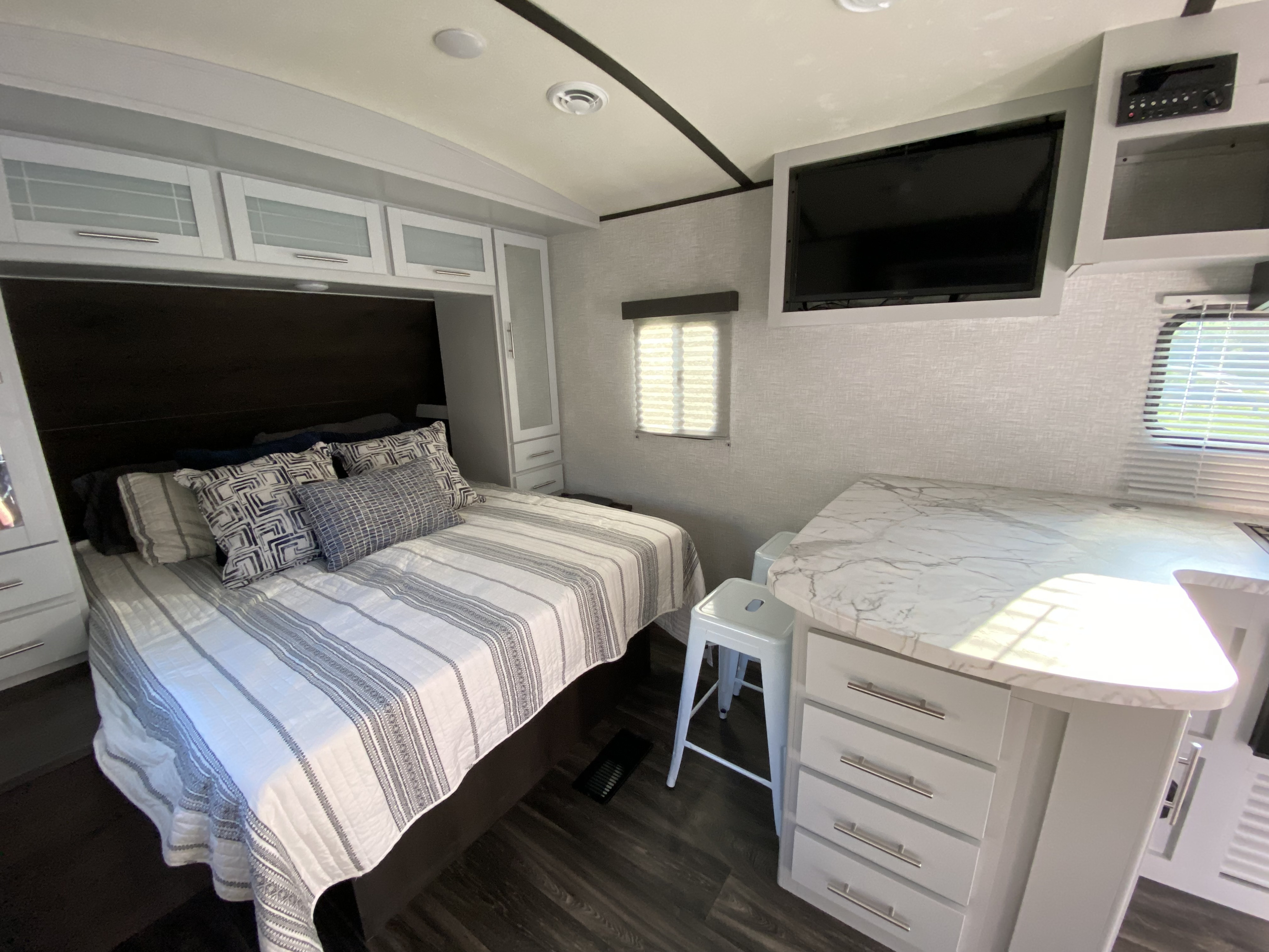 Modern RV rental interior with a cozy bed, white cabinetry, marble-style countertop, and mounted TV.. Keystone RV Bullet Ultra Lite 2021