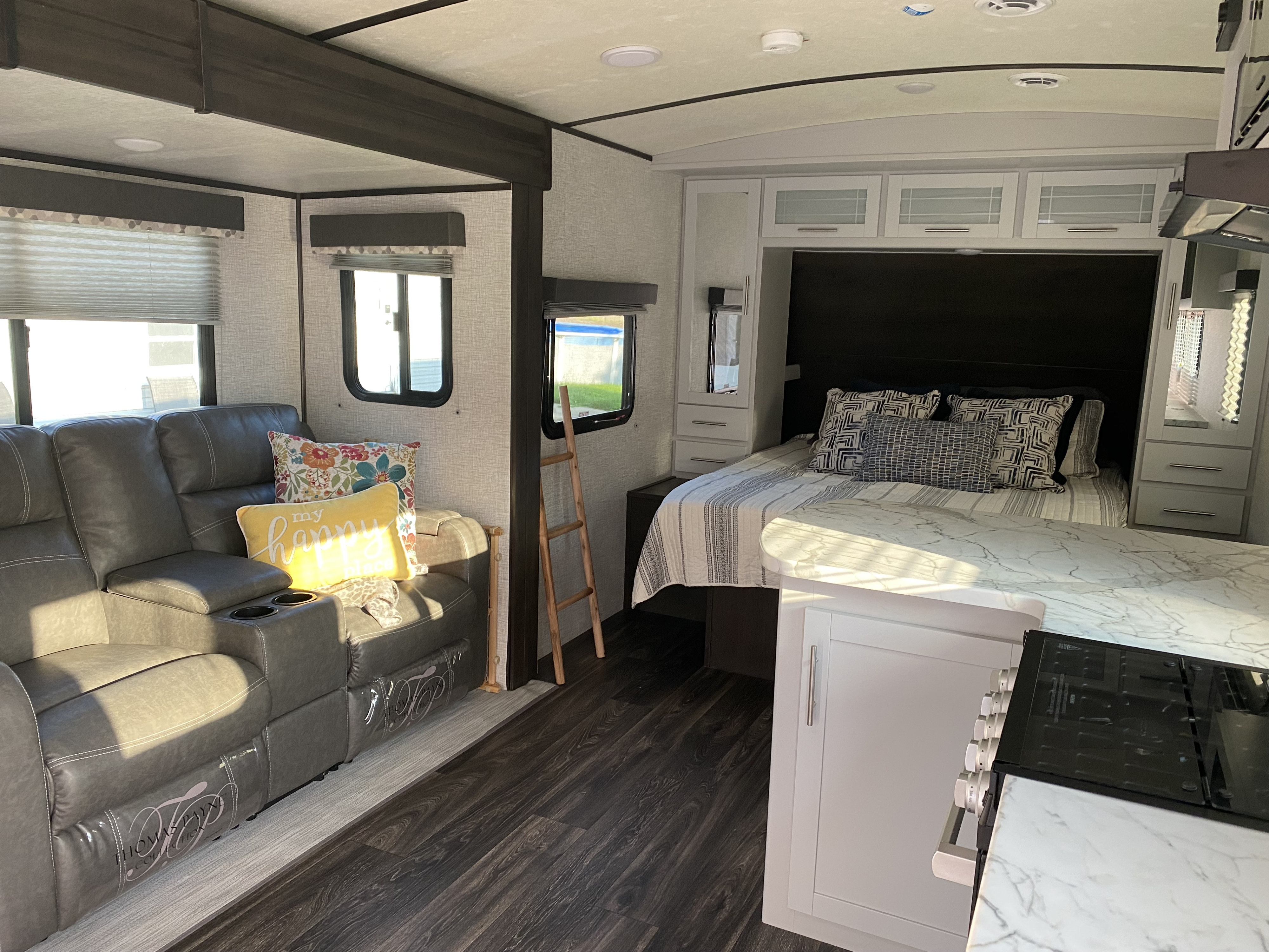 Inside this modern RV rental: a gray reclining sofa, queen bed, and kitchen area with white counters. Ideal for trips.. Keystone RV Bullet Ultra Lite 2021