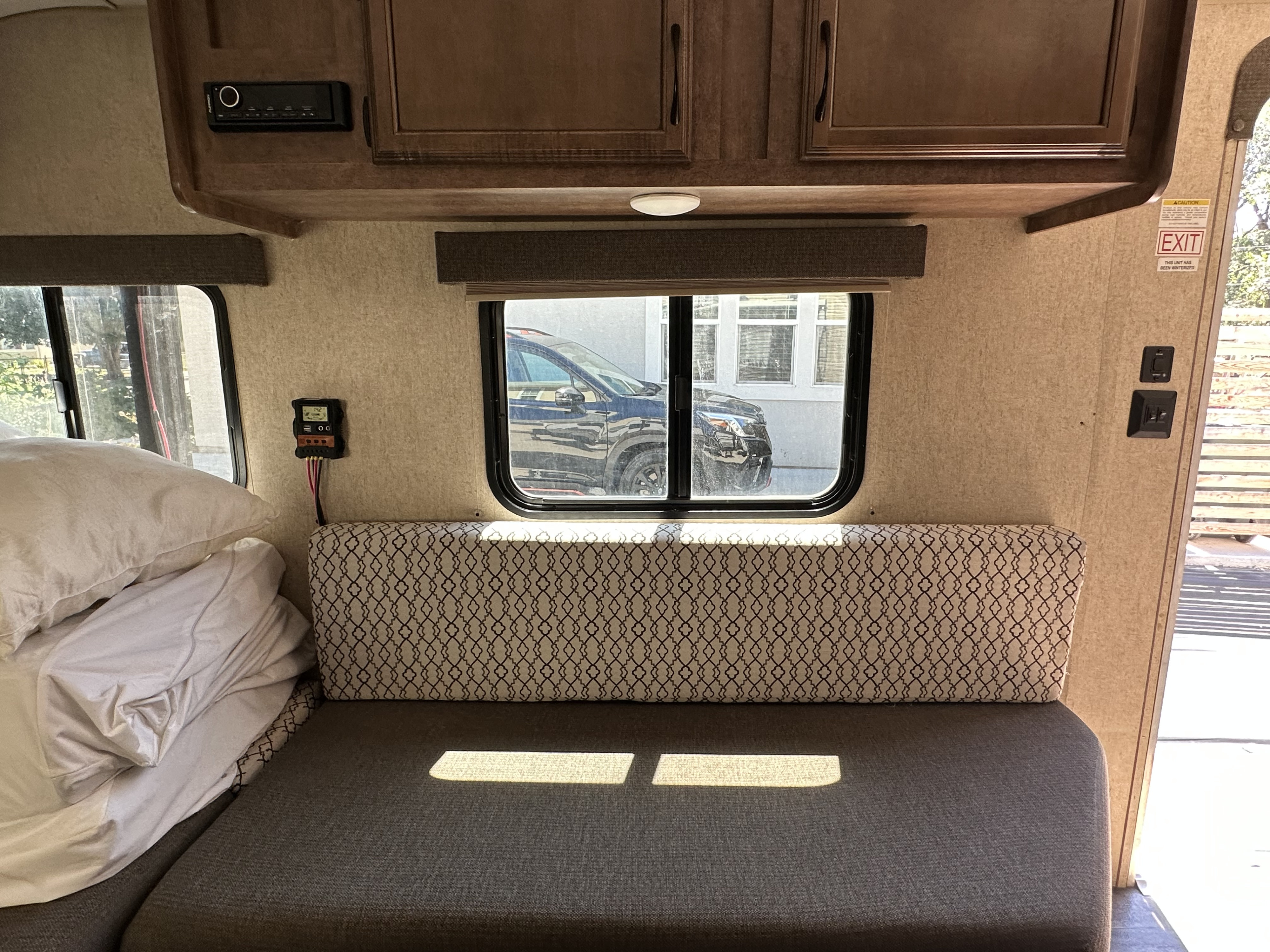 RV rental interior with a comfortable bed/seating area, overhead cabinets, and entertainment system. Solar controller and window view visible.. Starcraft Autumn Ridge 2018