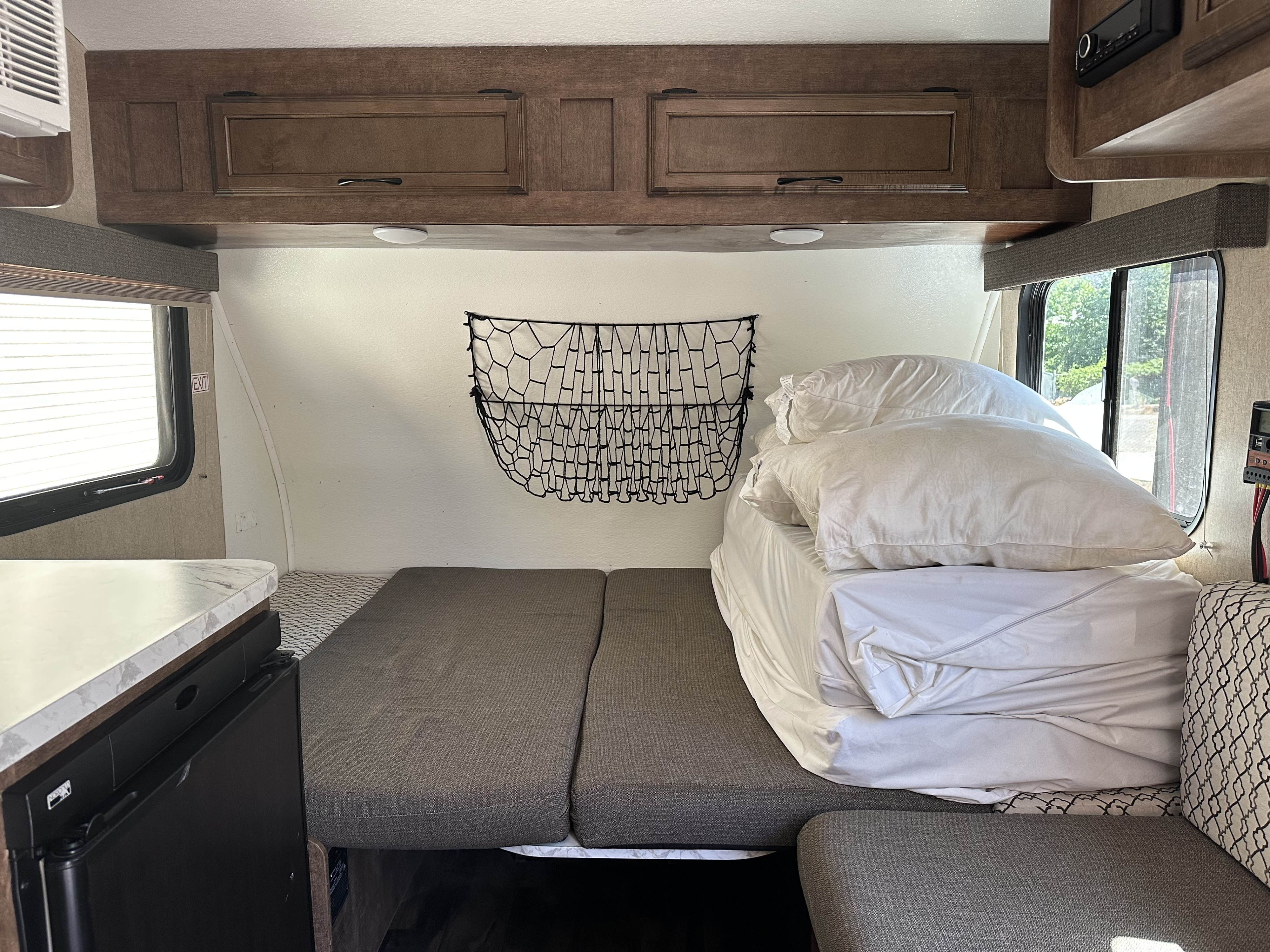 RV rental interior features a neatly made bed with white linens, wooden overhead cabinets, and a side window, ready for travel.. Starcraft Autumn Ridge 2018