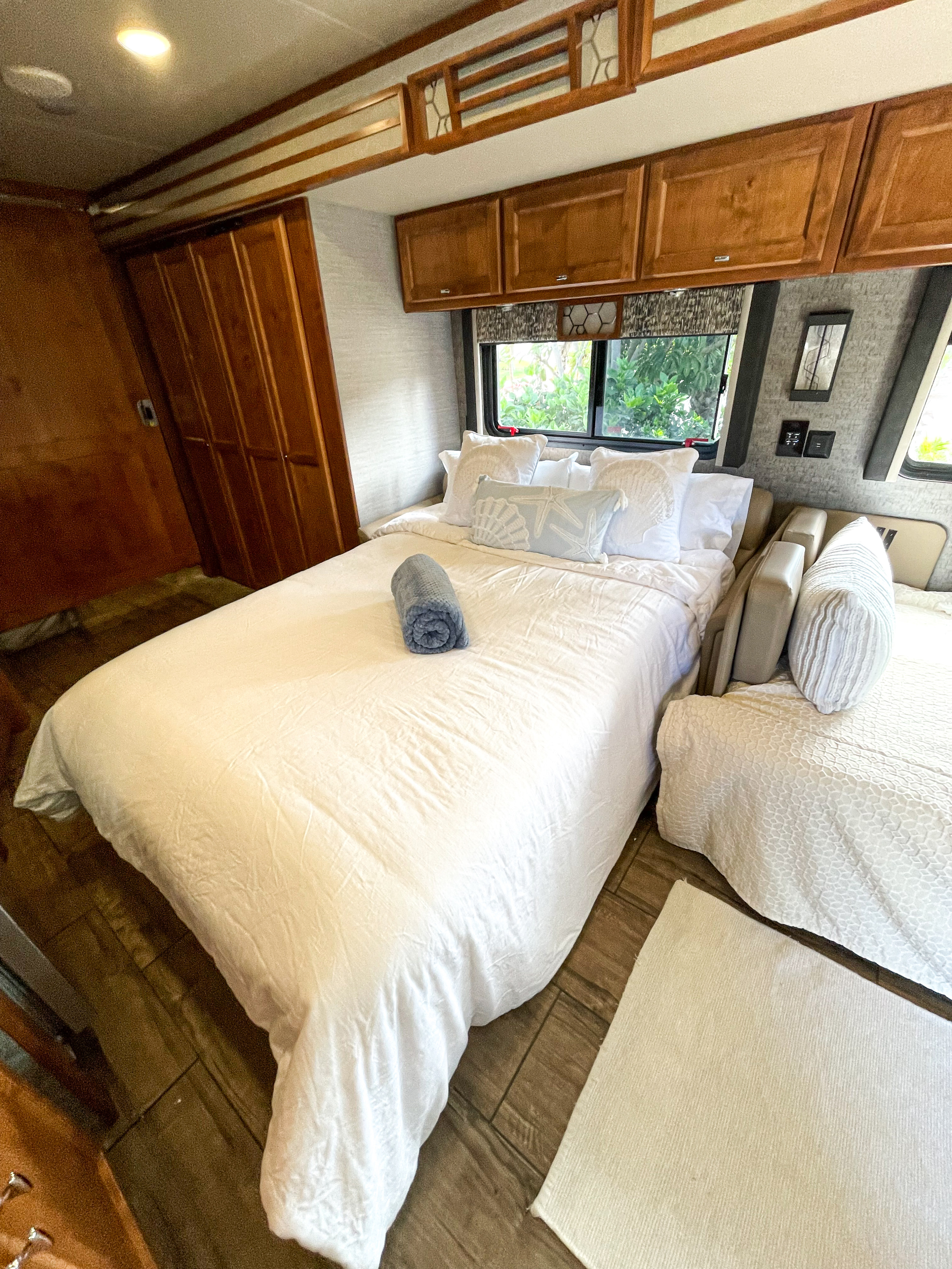 Cozy RV rental bedroom featuring a large bed with white linens, wooden cabinetry, and bright windows with natural light.. Tiffin Motorhomes Allegro Open Road 2020
