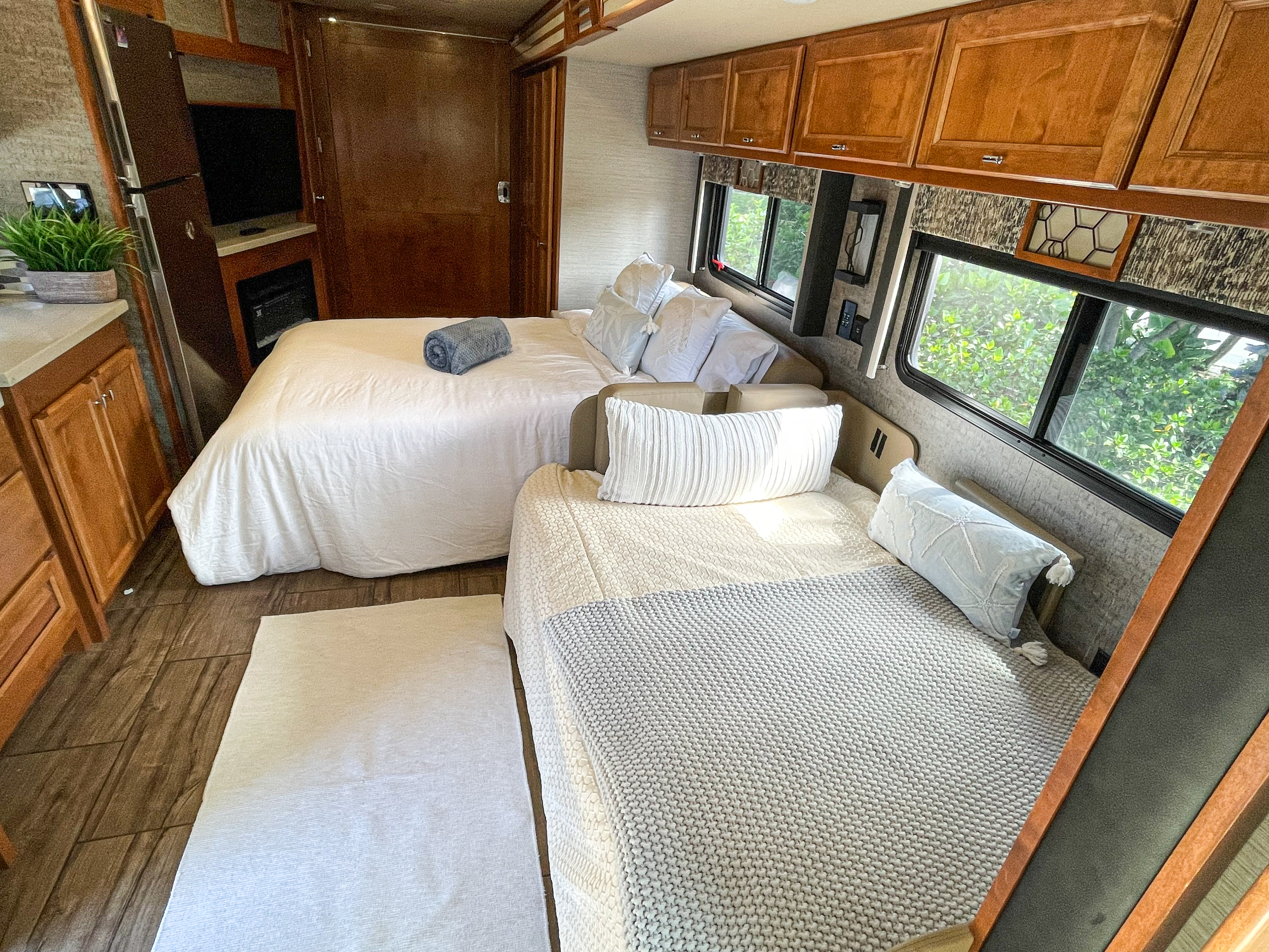 The inviting interior of an RV rental features two beds, a small kitchen area, and a TV.. Tiffin Motorhomes Allegro Open Road 2020