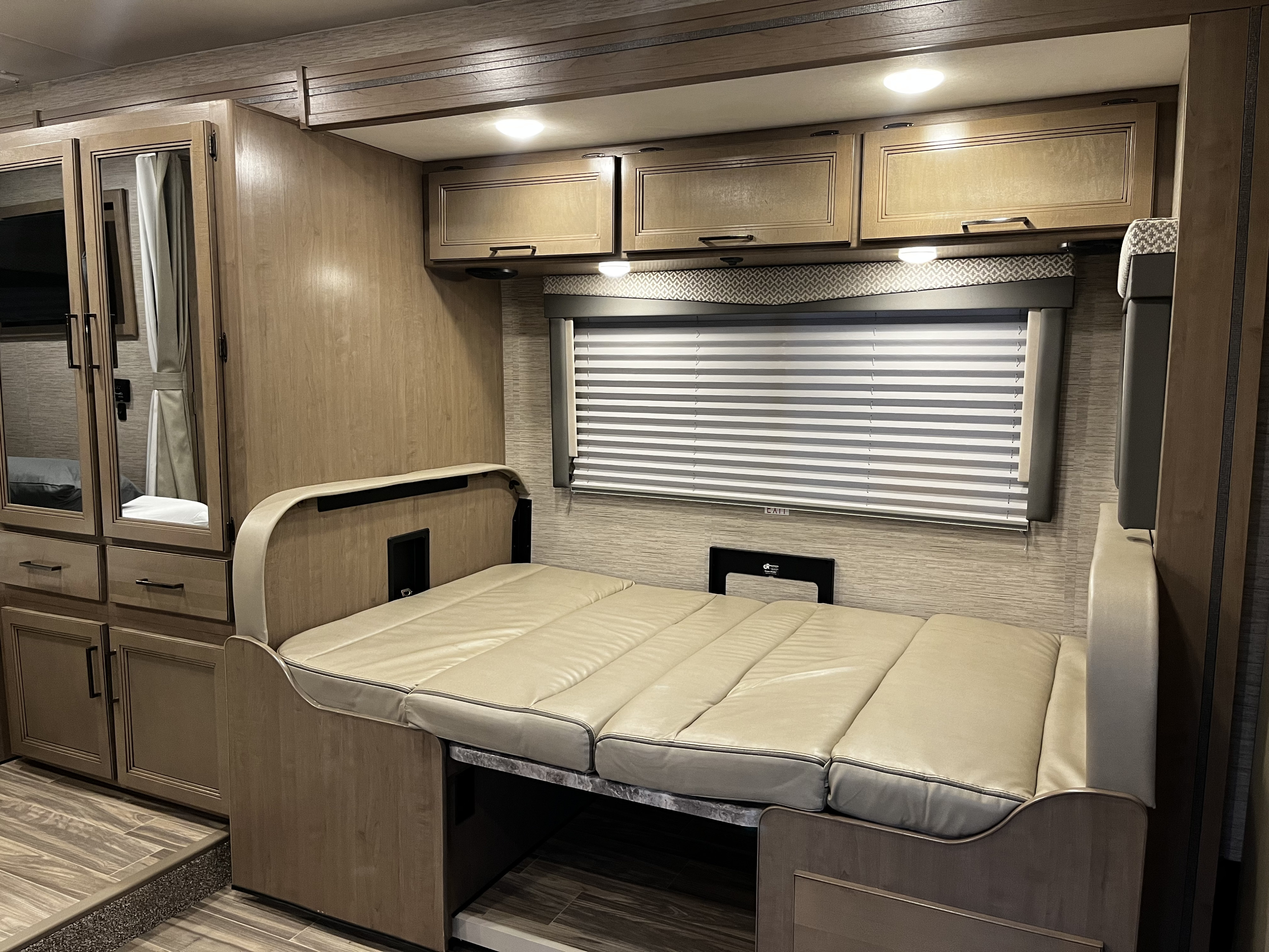 RV rental interior with a convertible bed, overhead cabinets, mirrored closet, and window blinds.. Thor Four Winds 2022