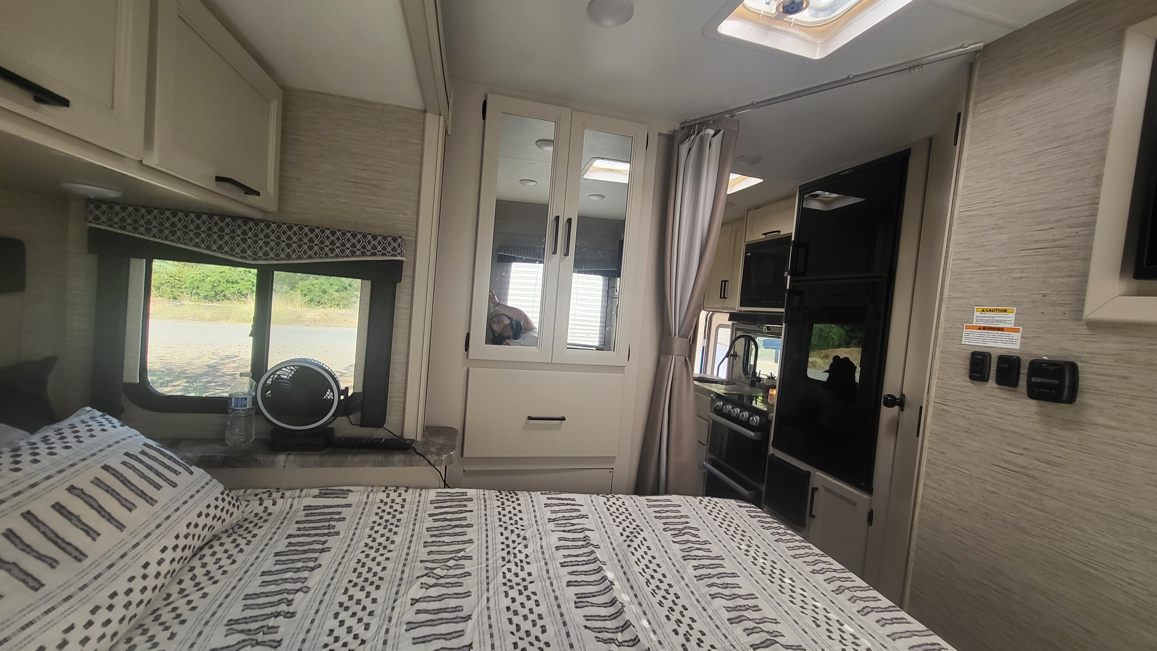 Discover this RV rental's interior: A cozy bedroom with patterned bed, mirrored storage, and compact kitchenette.. Thor Four Winds 2023