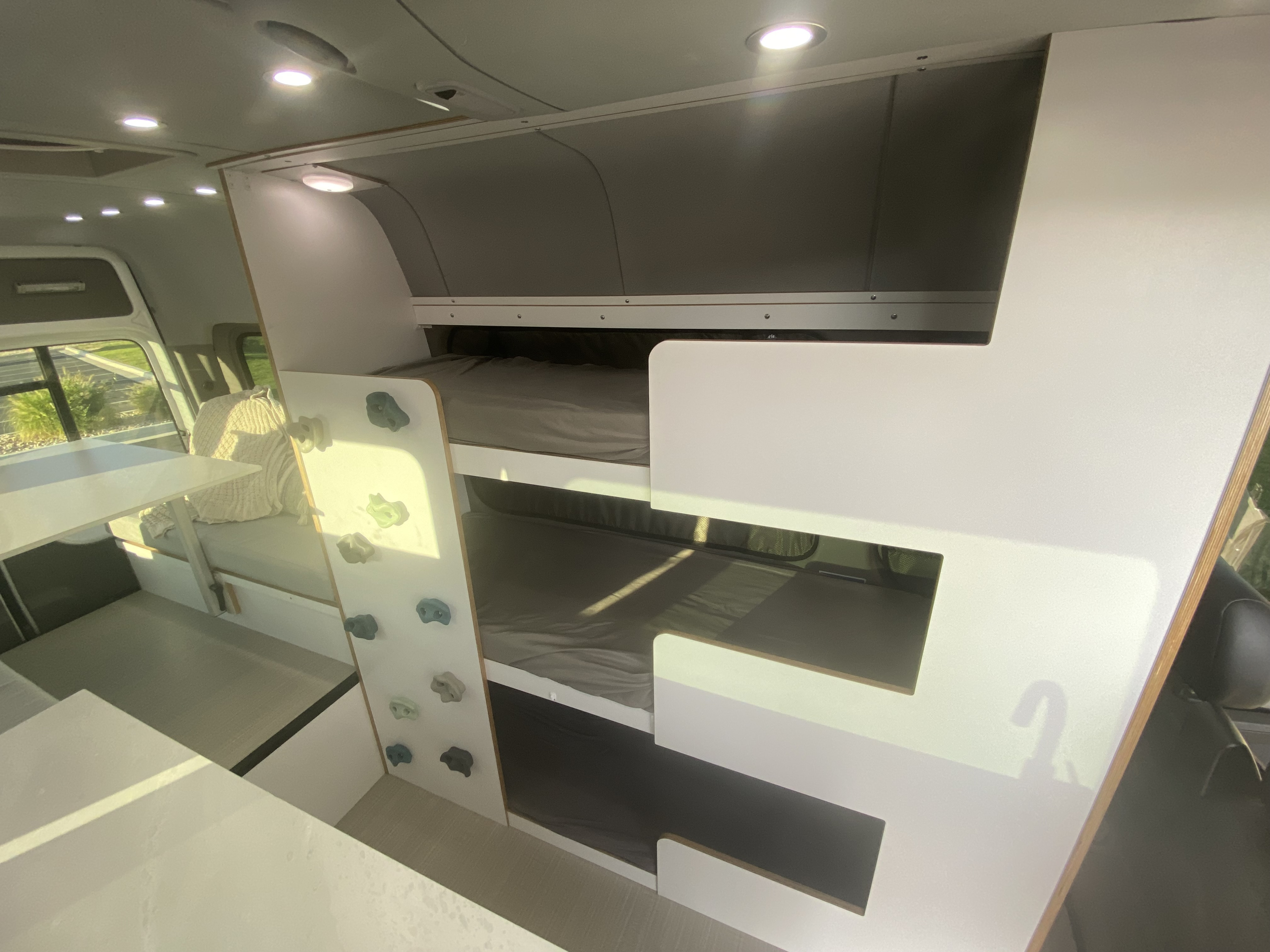 Inside a modern **rv rental**: bunk beds with a fun climbing wall, plus a comfortable dining/seating area.. Mercedes-Benz Sprinter 2014