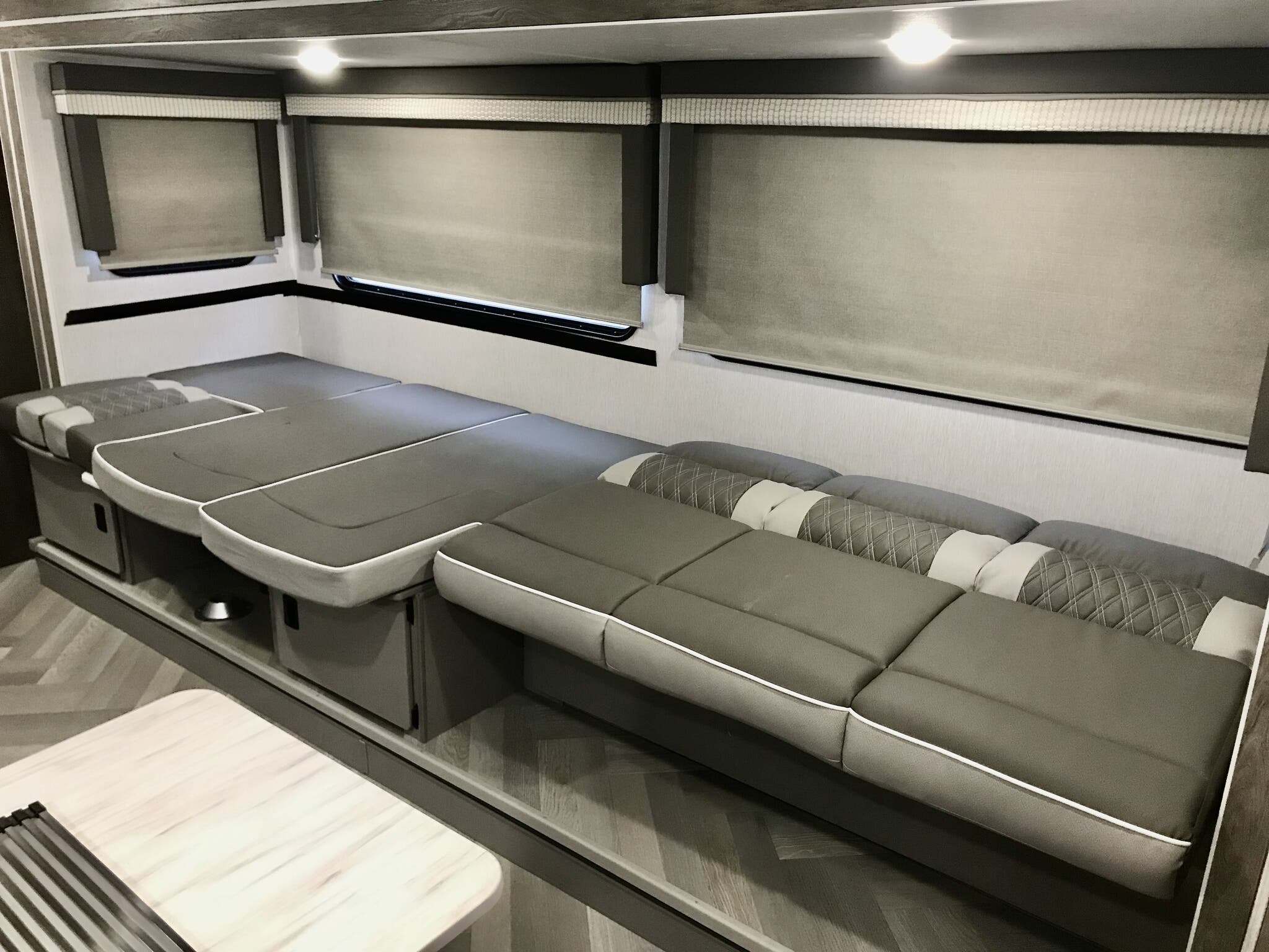 Versatile RV rental interior: grey sofa converts to bed, featuring large windows with shades and bright overhead lights.. Forest River Wildwood X-Lite 2023