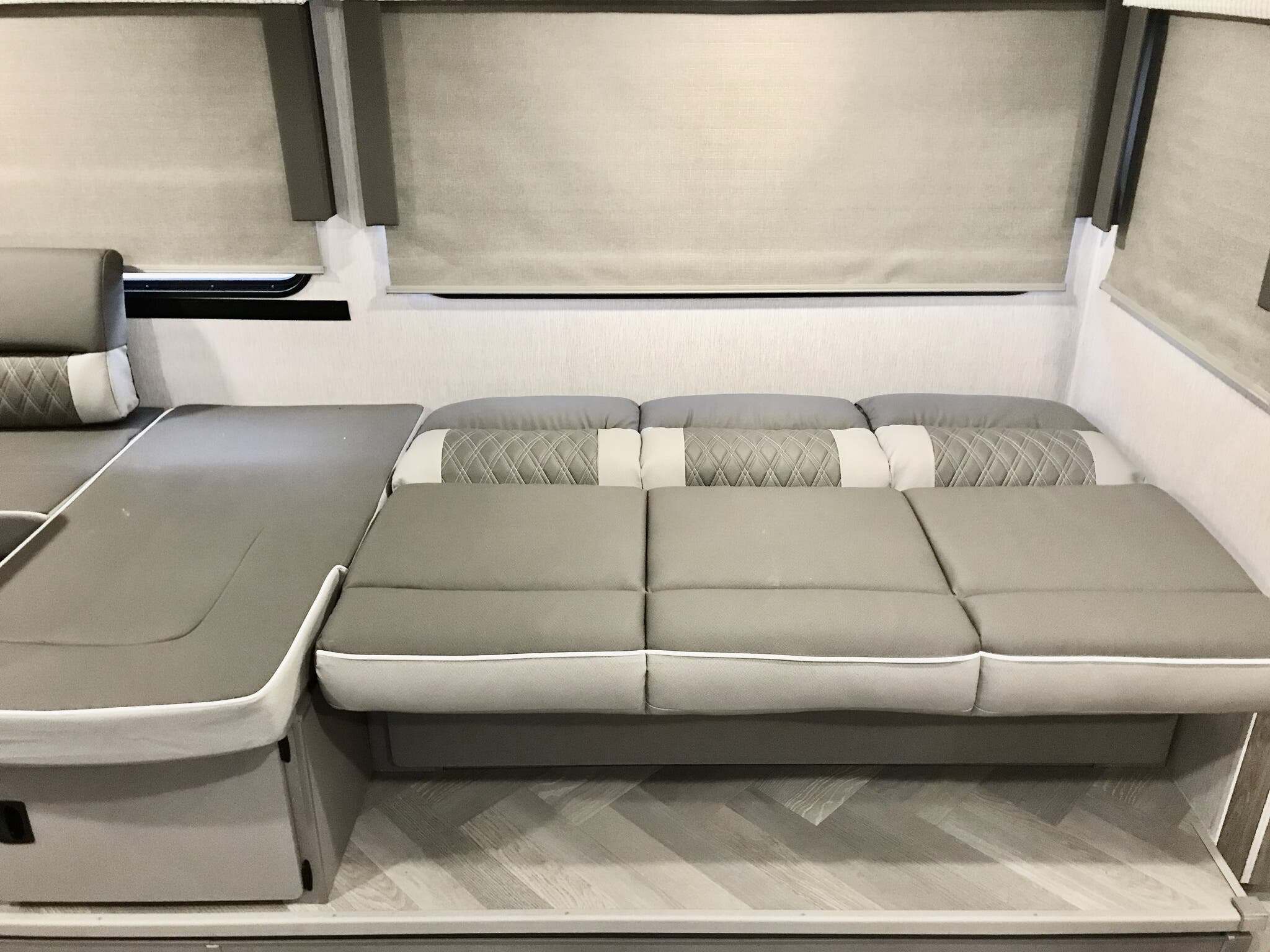 RV rental interior: L-shaped gray convertible seating with quilted backrests & blinds, ready for comfort.. Forest River Wildwood X-Lite 2023