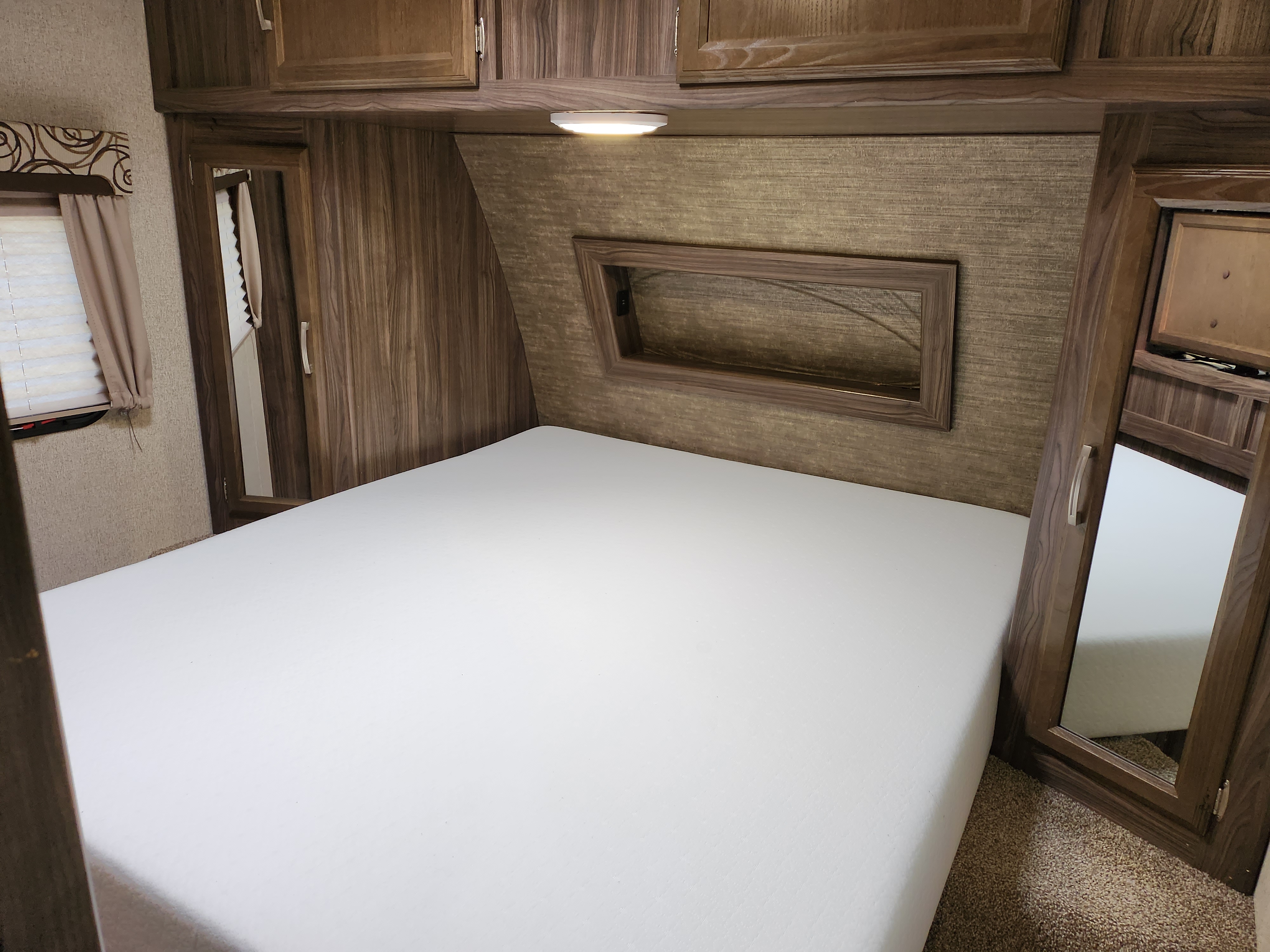 RV rental bedroom: A bright, clean space with a large white bed, warm wood cabinetry, and integrated mirrors.. Coachmen Apex 2017