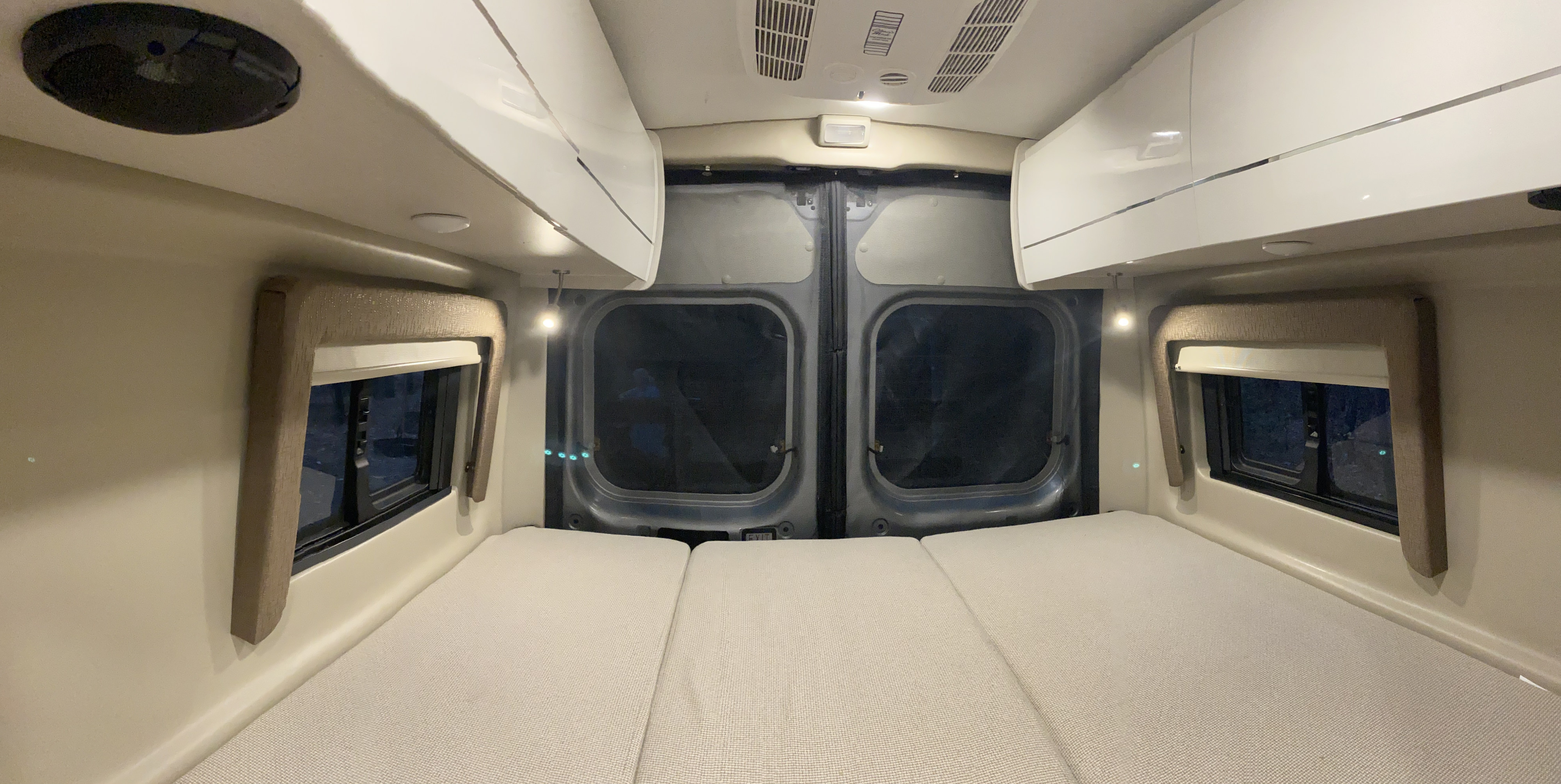 Inside an RV rental: a cozy sleeping area with three laid-out mattresses, side windows, and overhead cabinets.. Thor Tellaro 2022