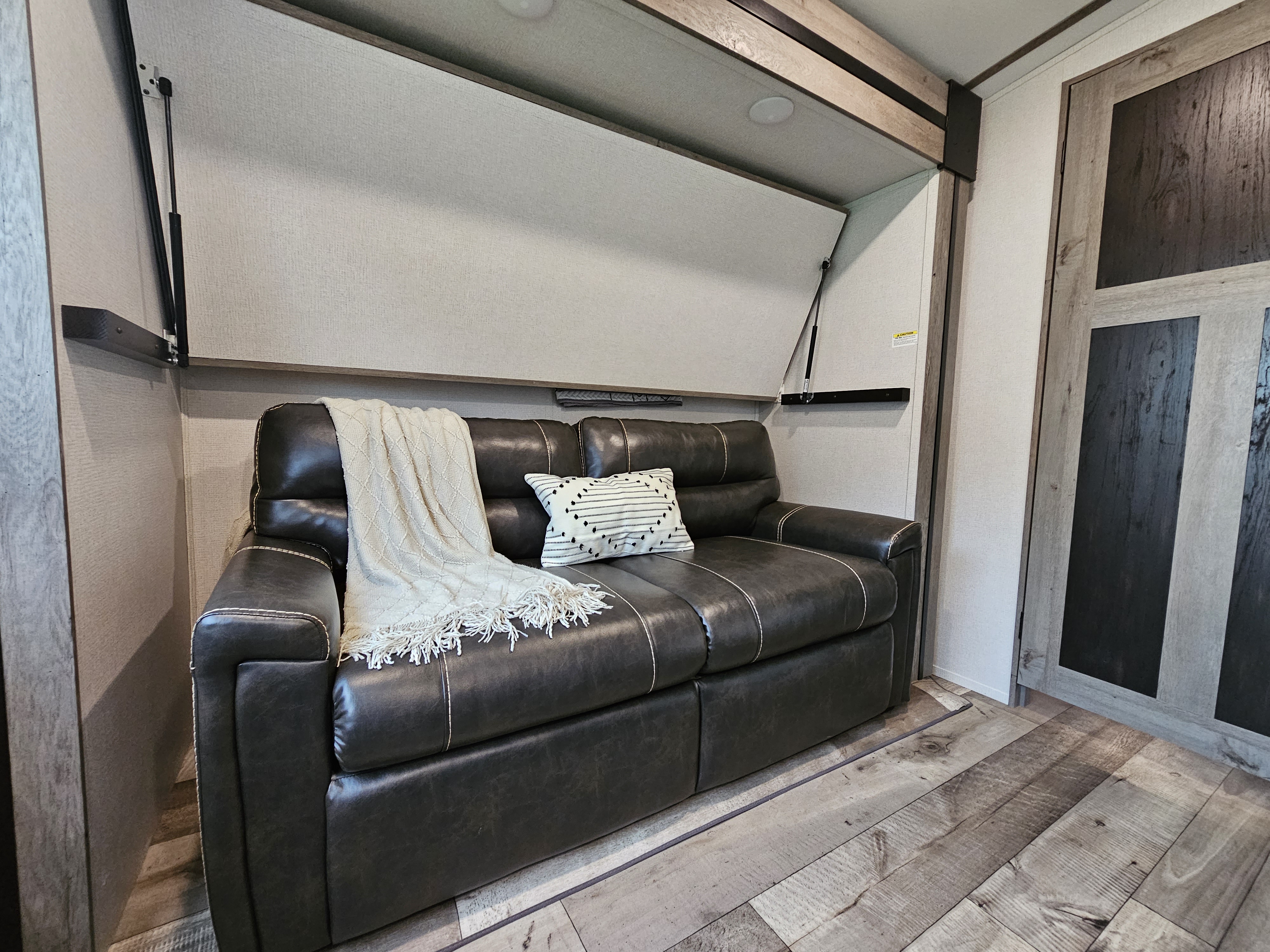 This RV rental offers a stylish, dark sofa with a cozy blanket, converting to a bed with overhead storage for efficient living.. Keystone RV Outback 2021