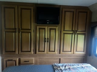 This RV rental bedroom features wall-to-wall wooden cabinets, a mounted TV, and a bed, creating efficient space.. Forest River Sunseeker 2011