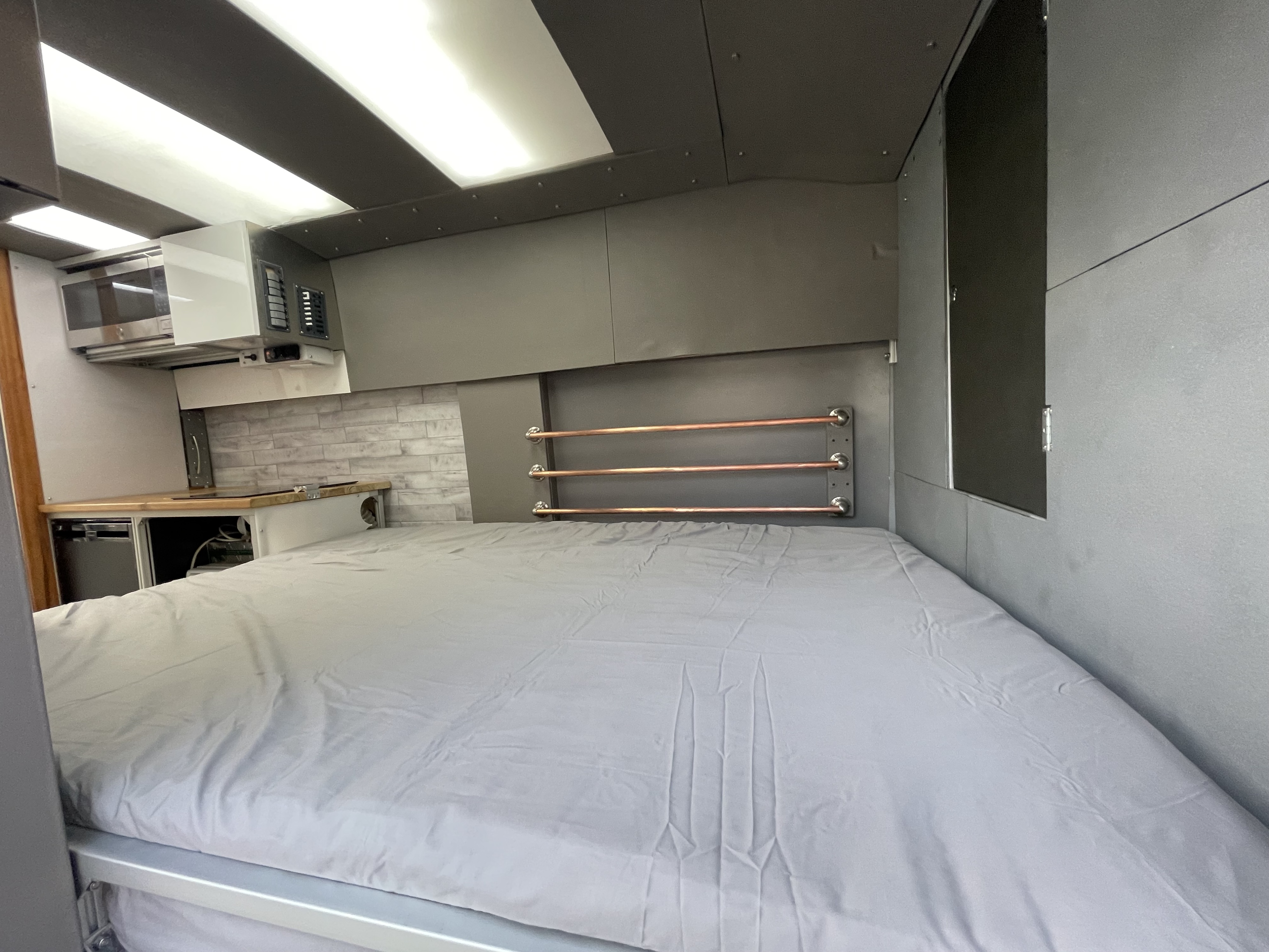 RV rental interior: a comfy bed, overhead cabinets, and a compact kitchen area with microwave and counter.. Other Transit 2022
