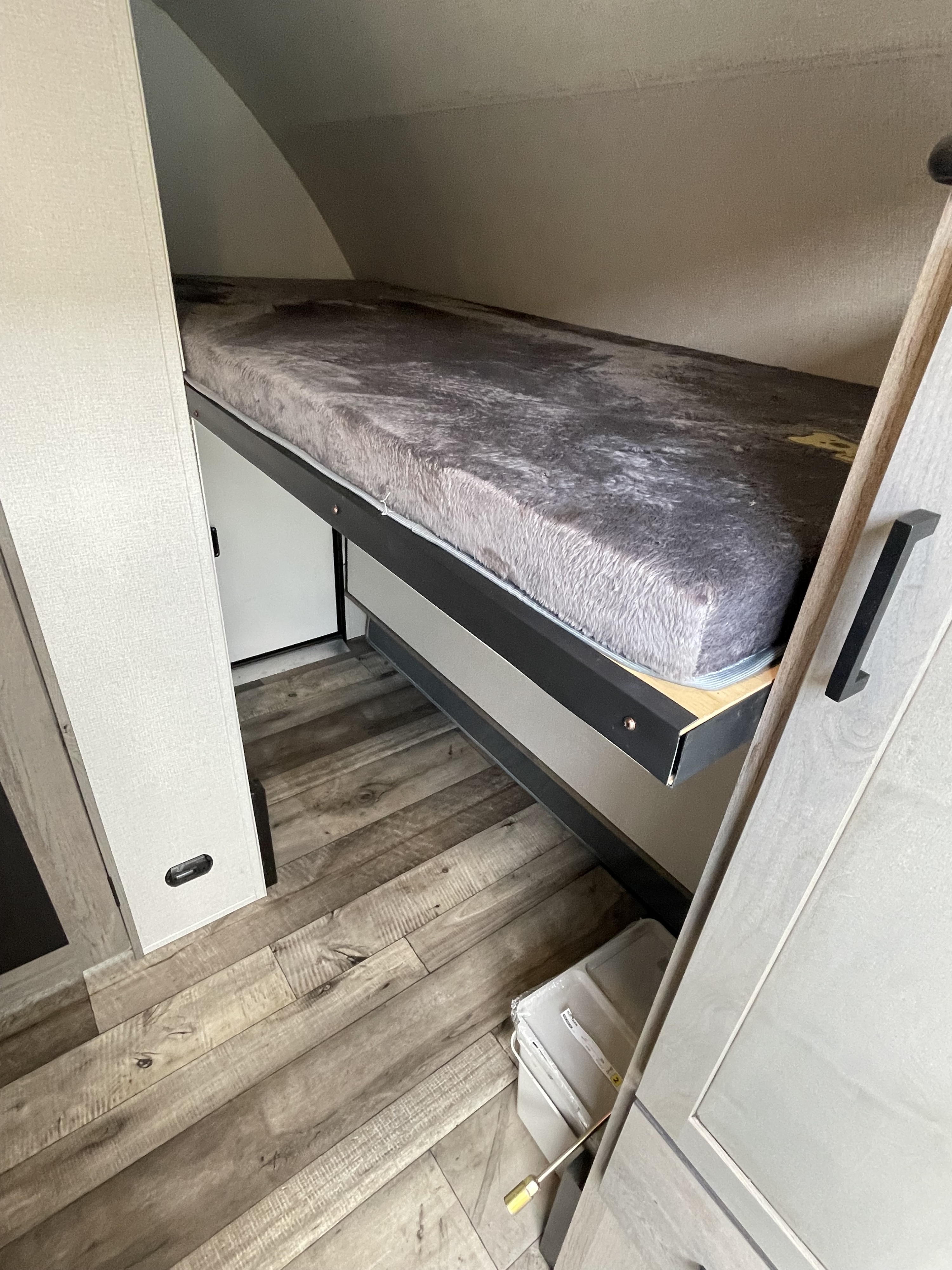 Cozy bunk bed with a plush grey mattress inside an RV rental, featuring practical wood-look flooring and compact design.. Keystone RV Outback Ultra-Lite 2021