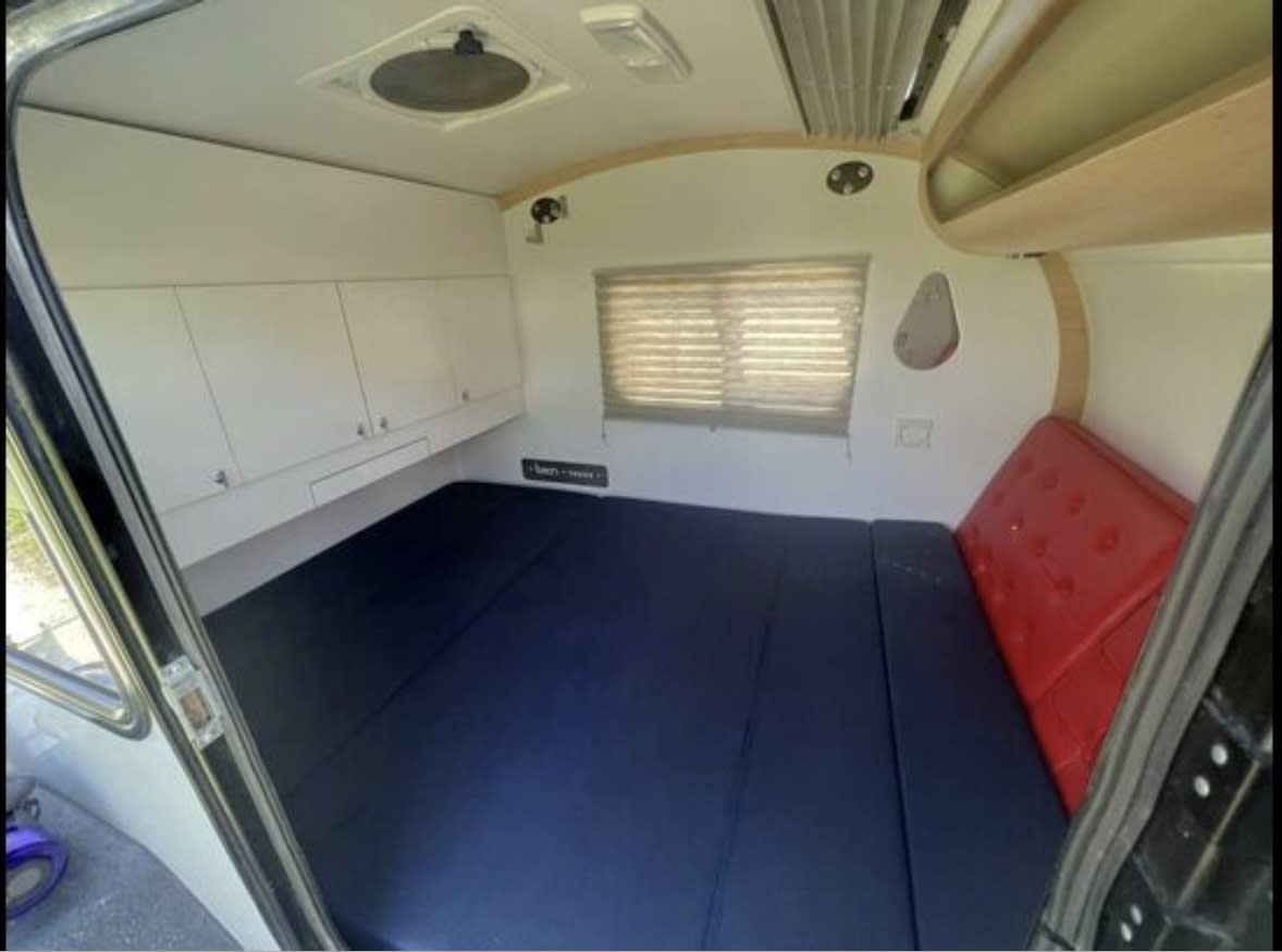 Inside an **rv rental**: compact sleeping area with a blue mattress, white cabinets, and a red headboard. Ready for adventure.. Bean Meaner Bean 2018