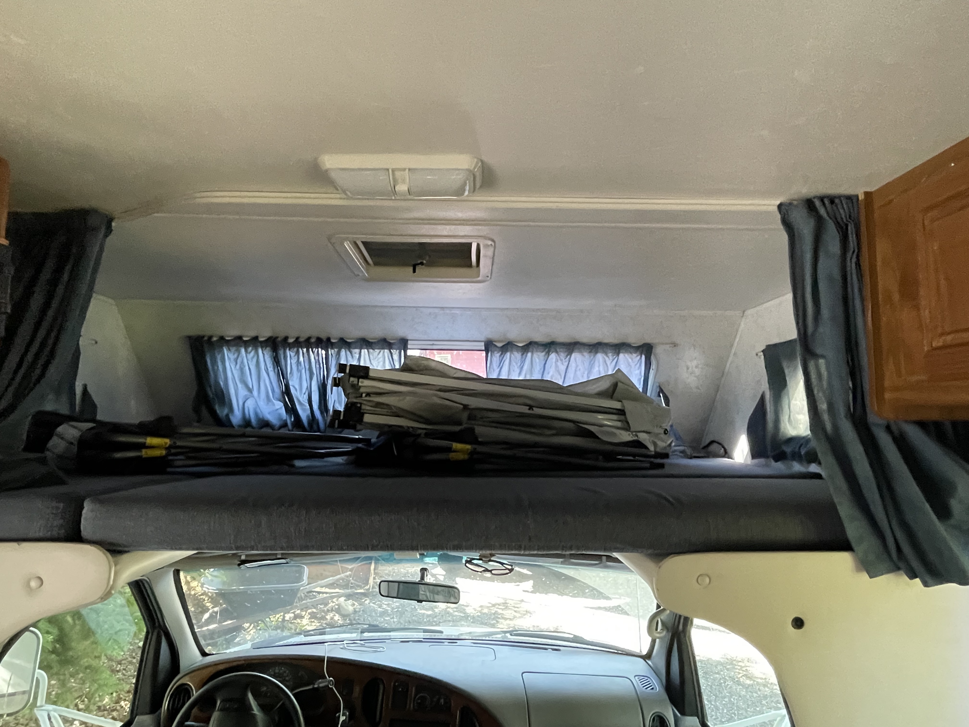 This RV rental's interior shows the overhead bunk bed with camping gear, ceiling light, and front windshield.. Dutchmen Express 2001