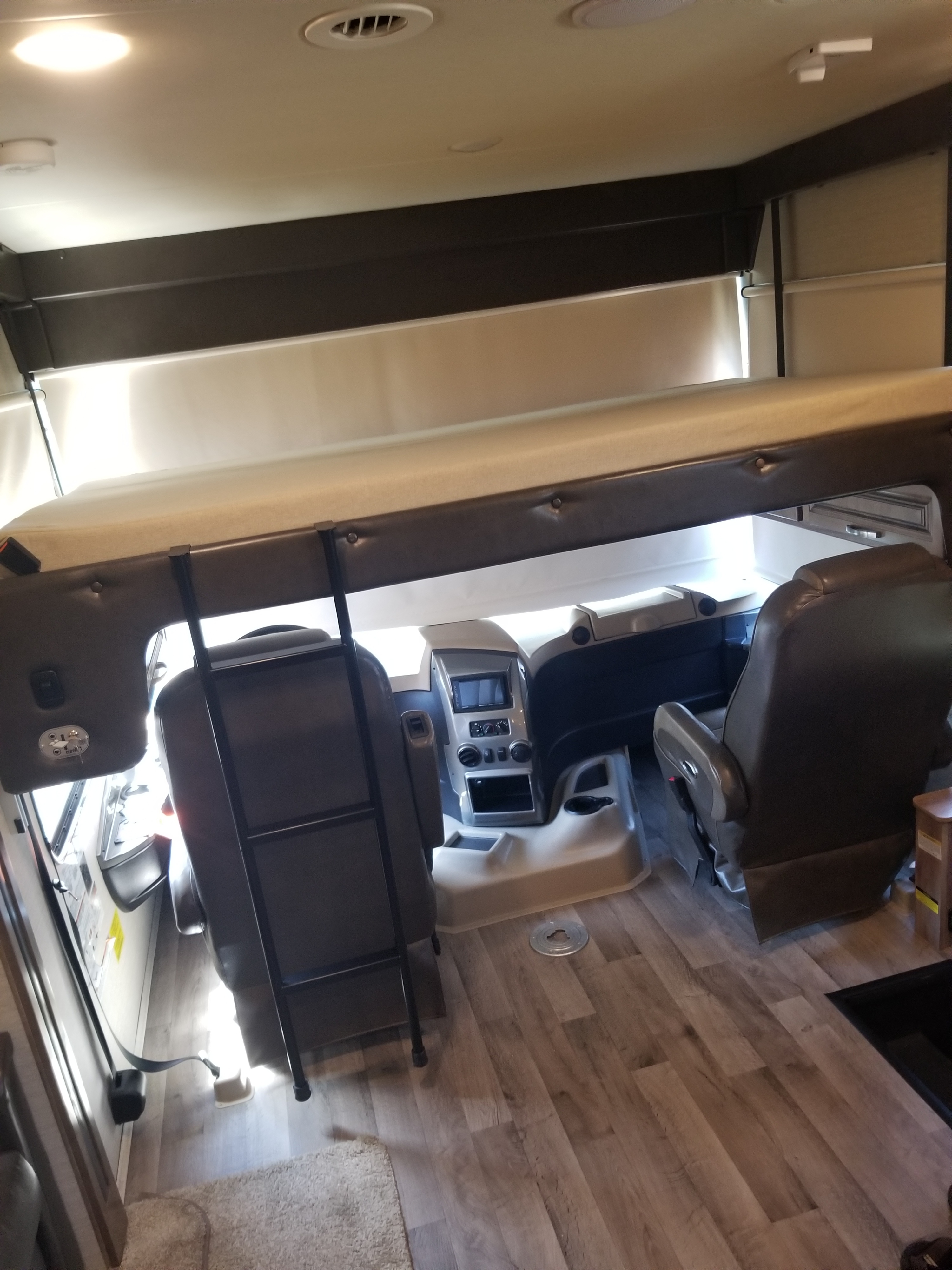 View of an rv rental's interior, showing the cockpit with driver/passenger seats and a lowered overhead bunk with ladder.. Jayco Precept Prestige 2019