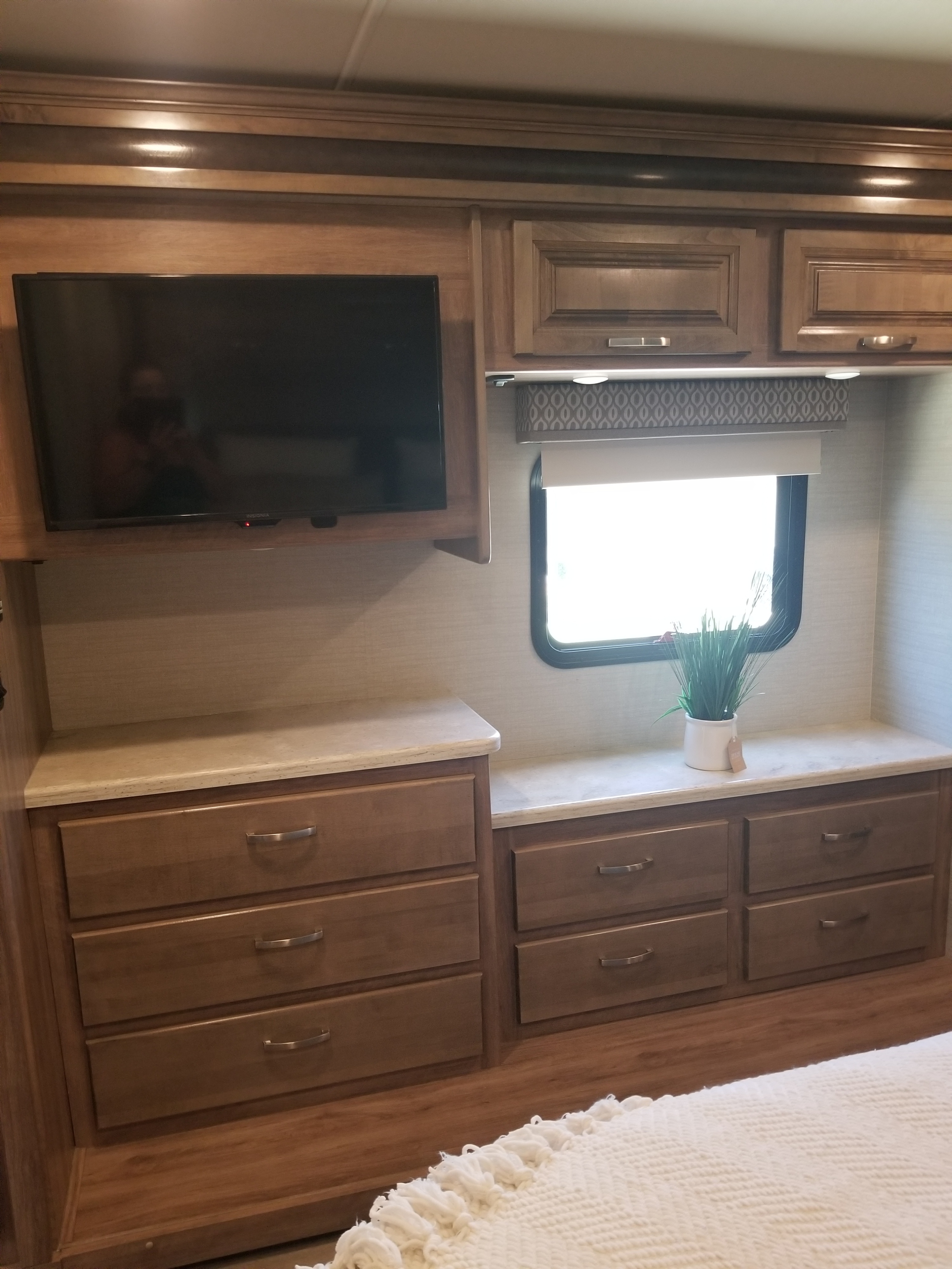 Cozy RV rental bedroom with TV, ample wooden storage drawers, and a window for natural light. Ideal for comfortable travels.. Jayco Precept Prestige 2019