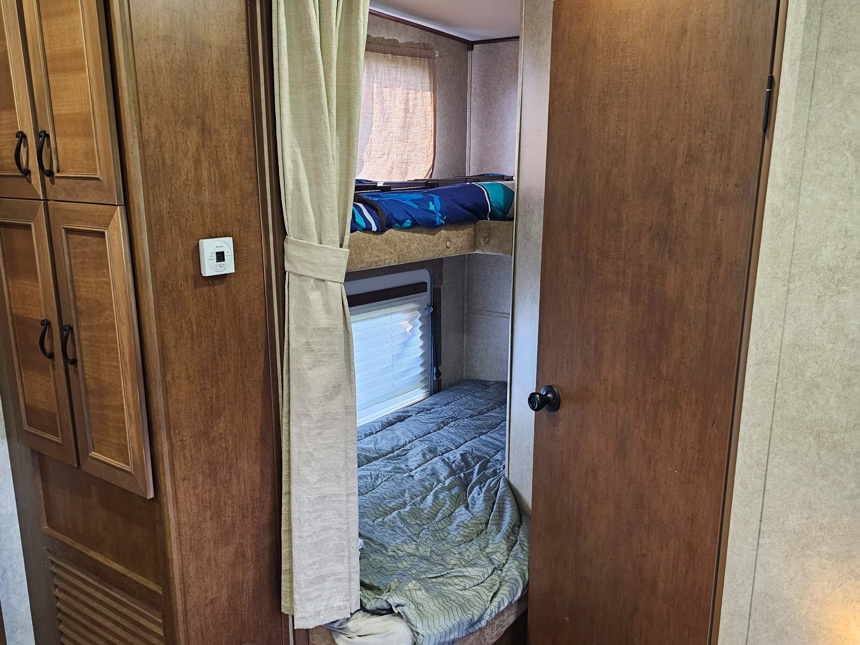 Cozy RV rental interior featuring bunk beds, wooden cabinets, and a side door, ideal for family sleeping areas.. Open Range RV Light 2014