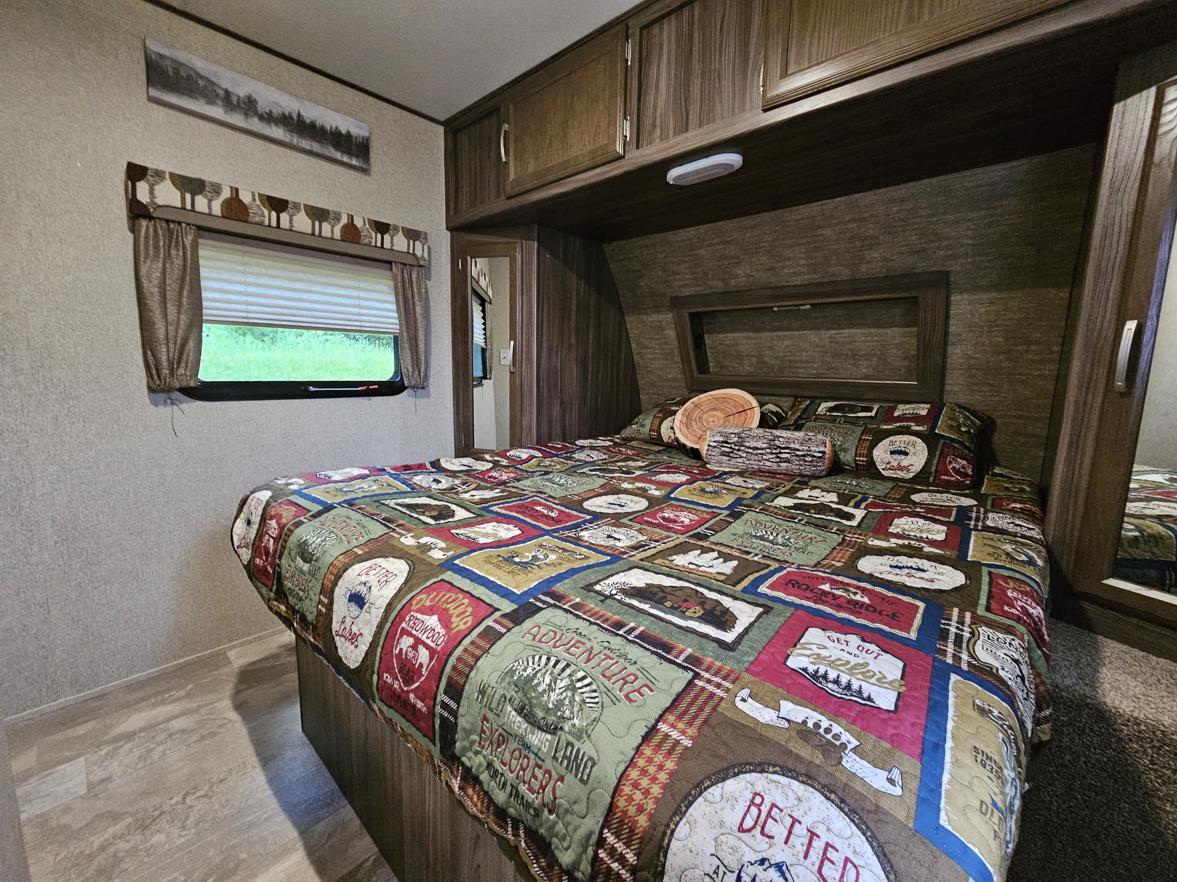 Cozy RV rental bedroom featuring adventure-themed bedding, log pillows, and ample storage. Perfect for a travel escape.. Coachmen Apex 2017