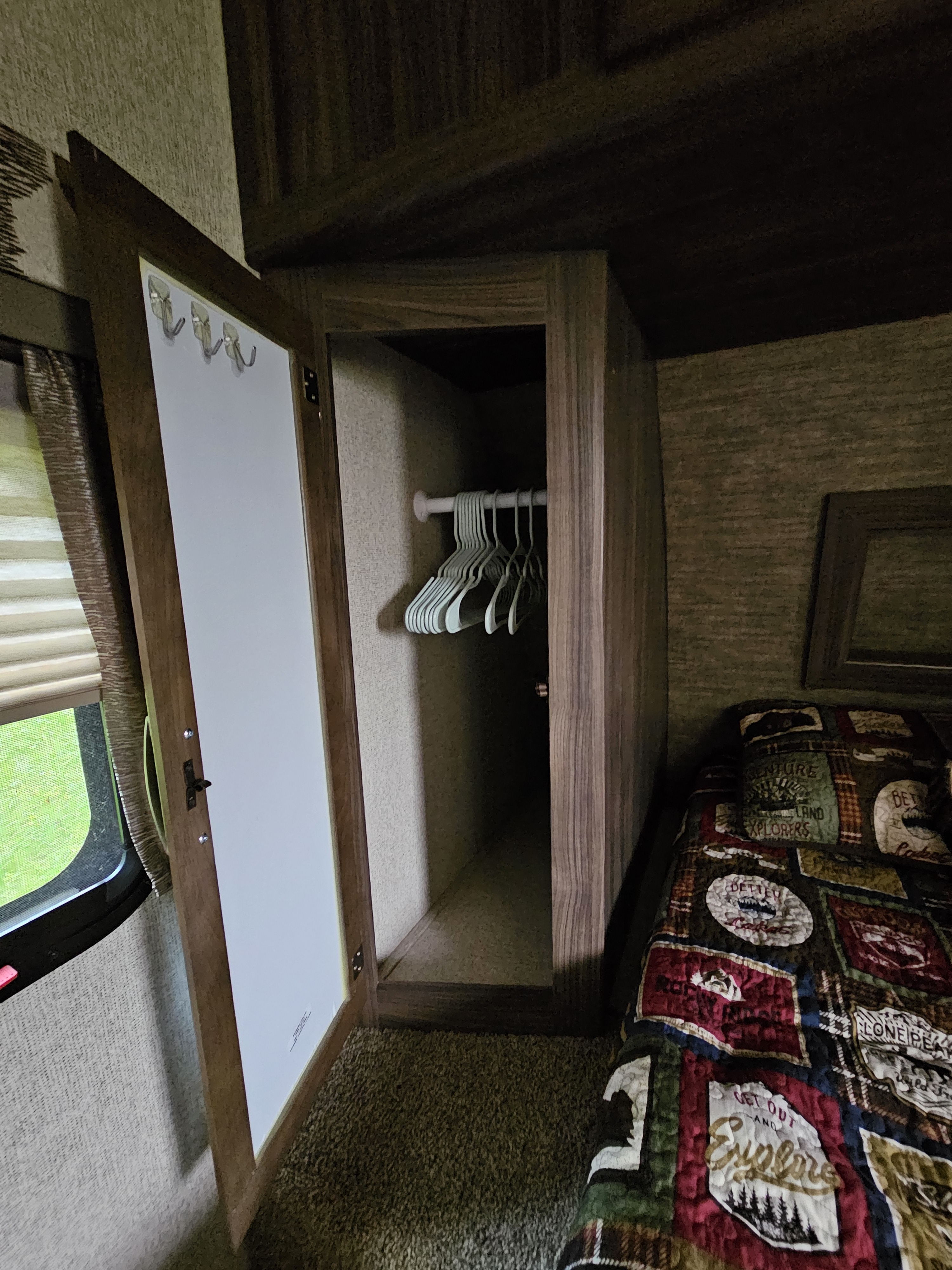 RV rental bedroom: Open closet with hangers, hooks on door, and a comfy bed with a patterned quilt, maximizing space.. Coachmen Apex 2017