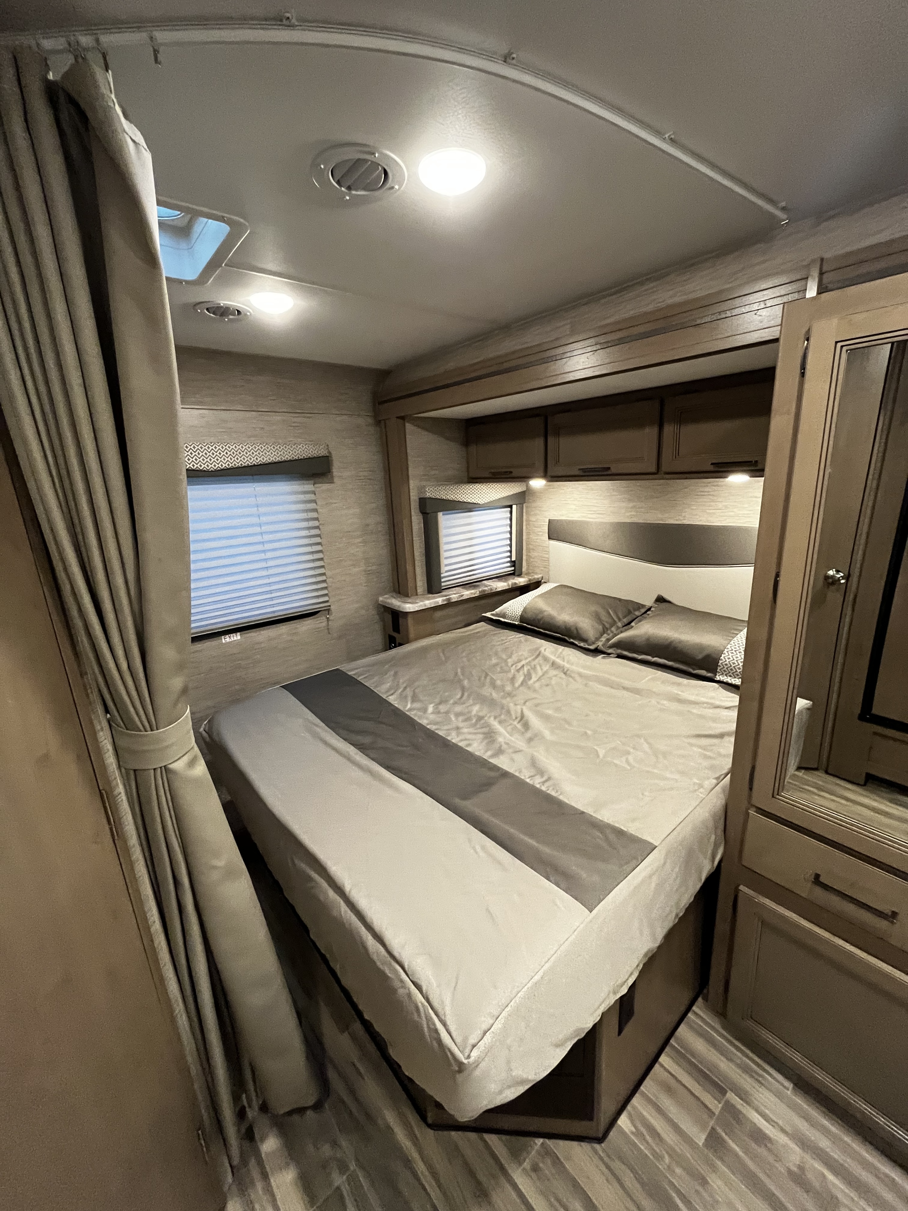 An inviting RV rental bedroom featuring a modern bed, windows, built-in cabinets, and warm lighting for your journey.. Thor Four Winds 2022