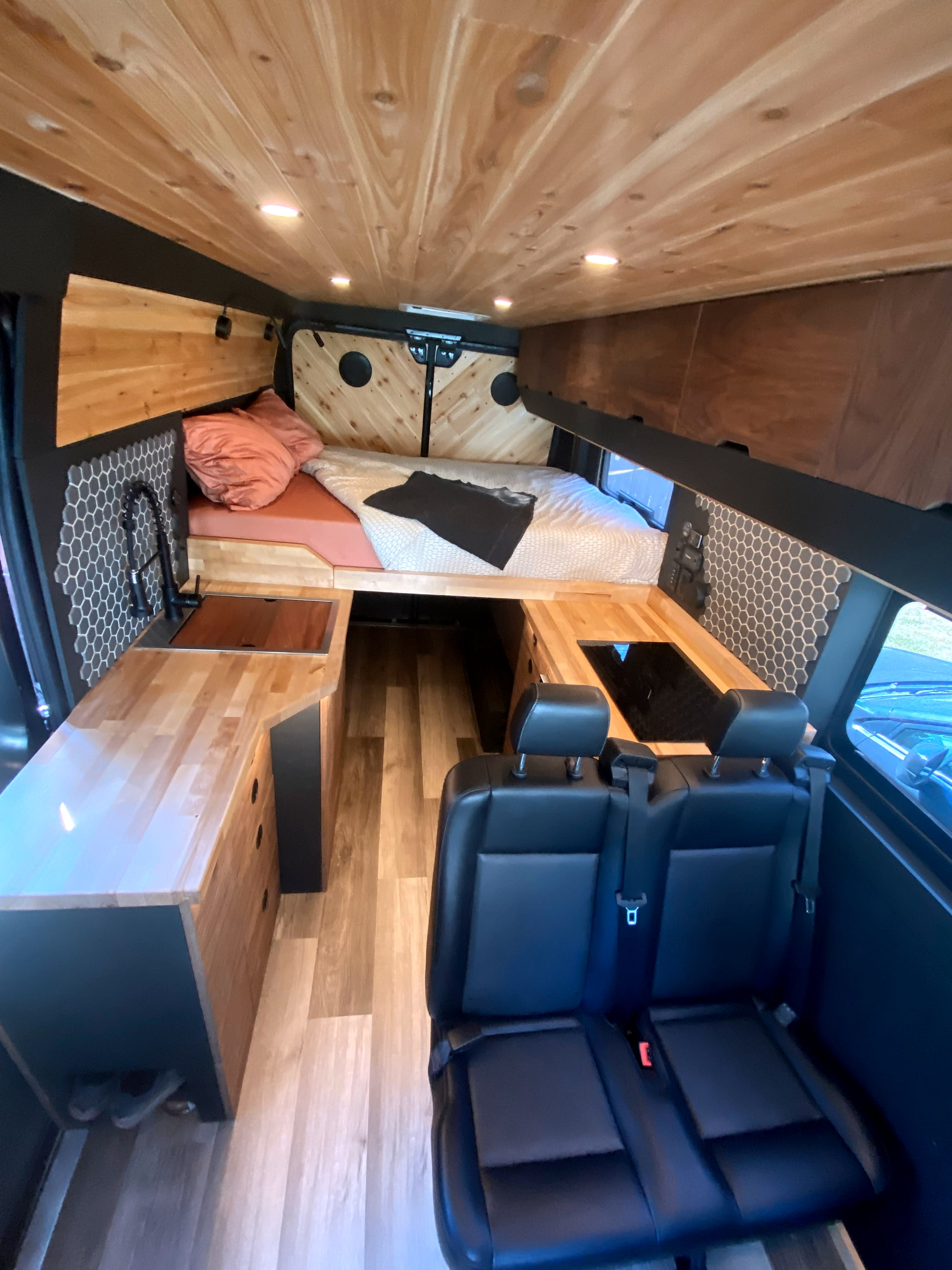 Stylish RV rental: wood-paneled ceiling, hexagon tiles, comfy bed, kitchenette, and passenger seating for adventure.. Ram Promaster 2019