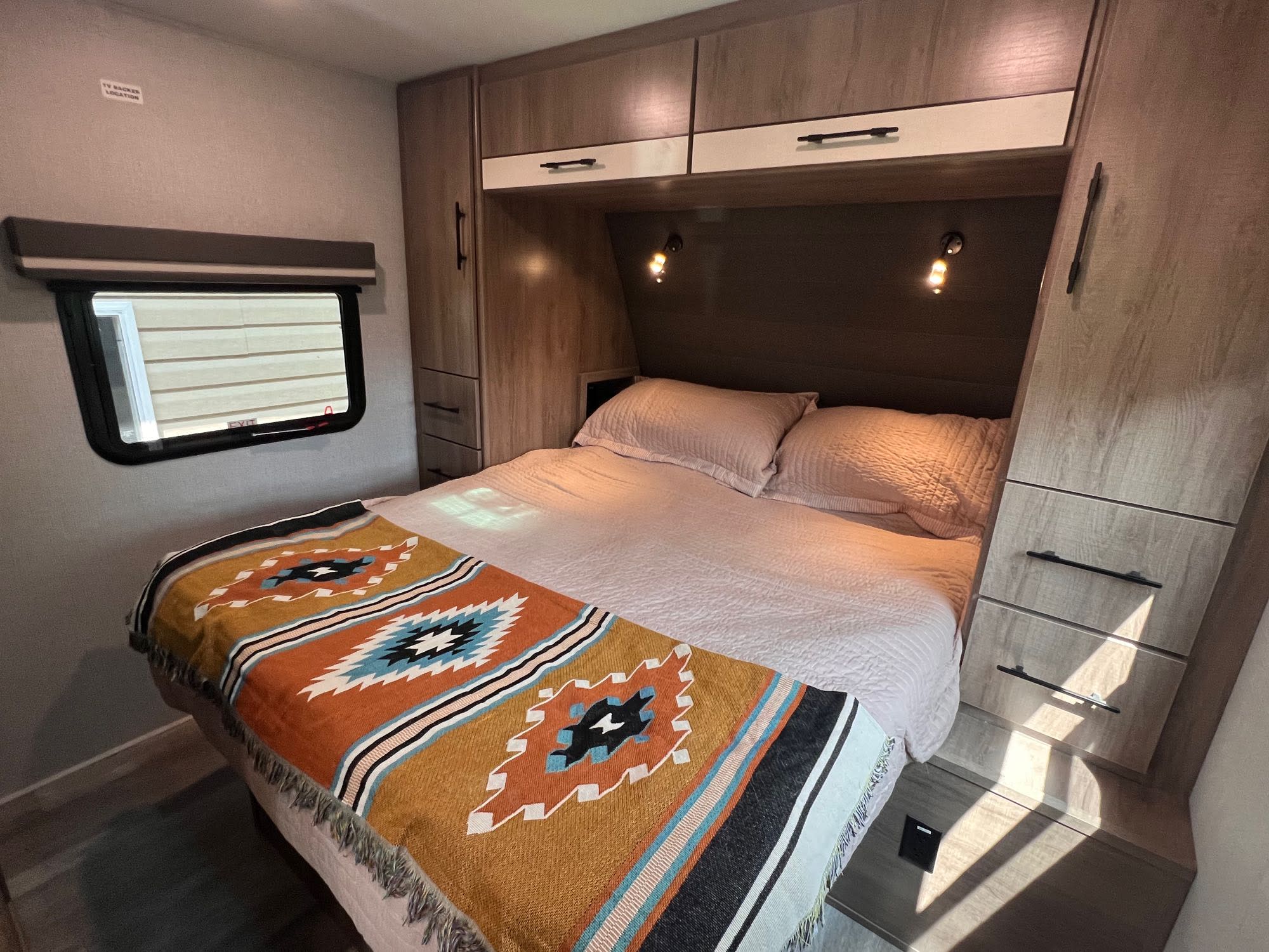 Cozy RV rental bedroom featuring a large bed, ample storage, and reading lights, designed for comfort on the road.. Grand Design Imagine XLS 2023