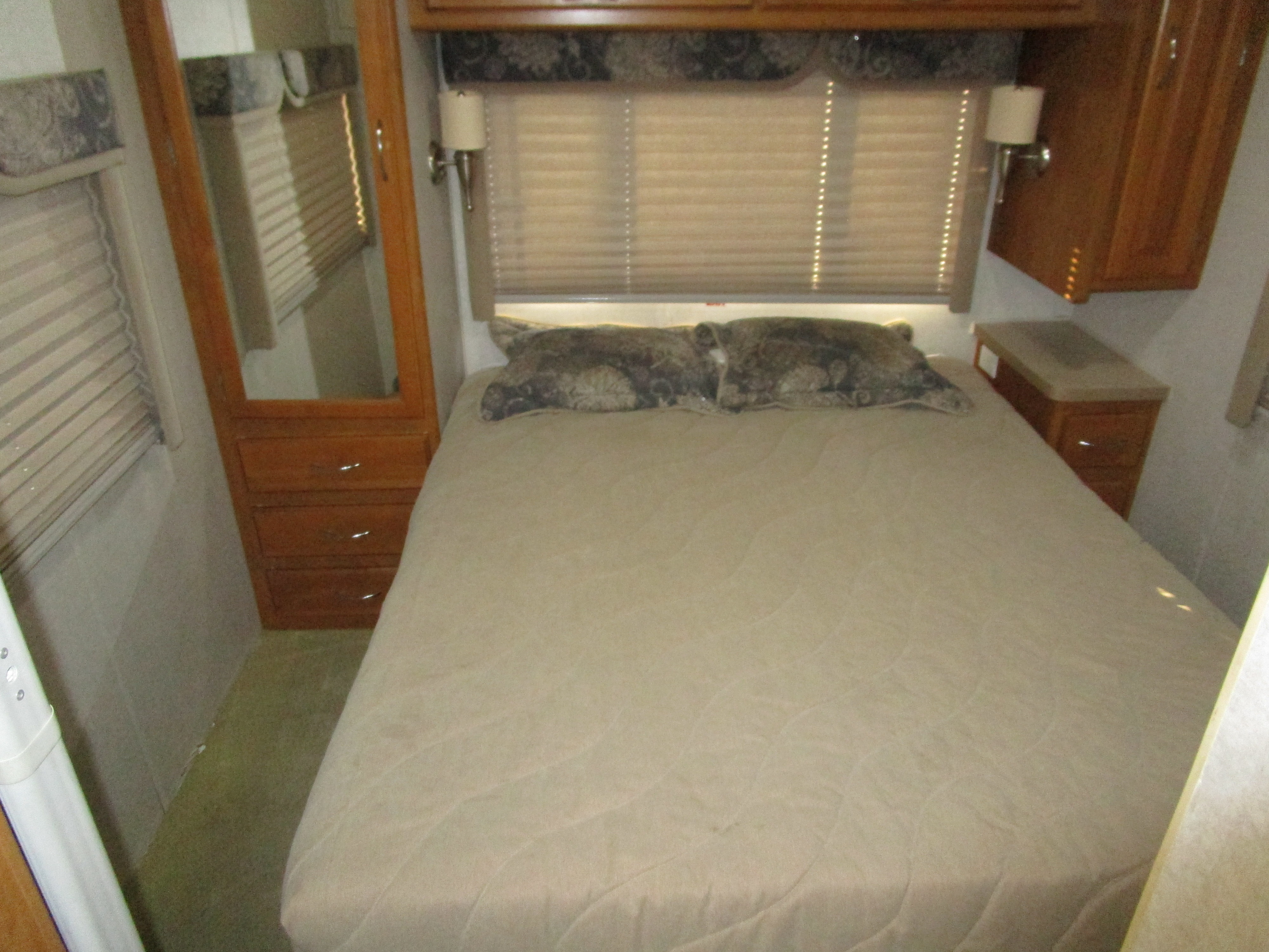 Compact RV rental bedroom featuring a bed, overhead cabinets, and a mirrored wardrobe with drawers. Ideal for journeys.. Jamboree Jamboree Motorhome 2002