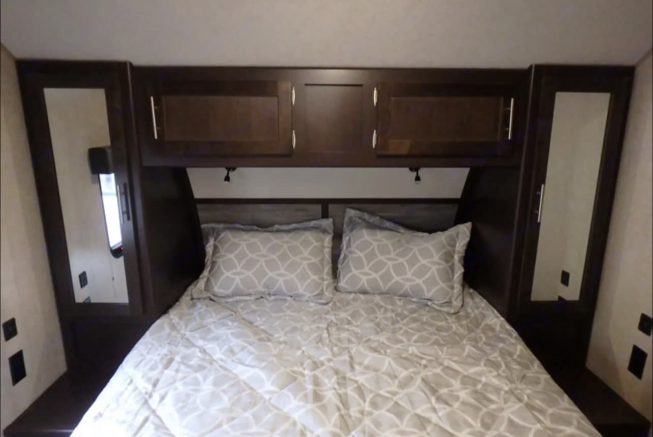 View inside an RV rental bedroom, showcasing a comfortable bed, dark wood overhead storage, and mirrored bedside wardrobes.. Forest River Cherokee 2018