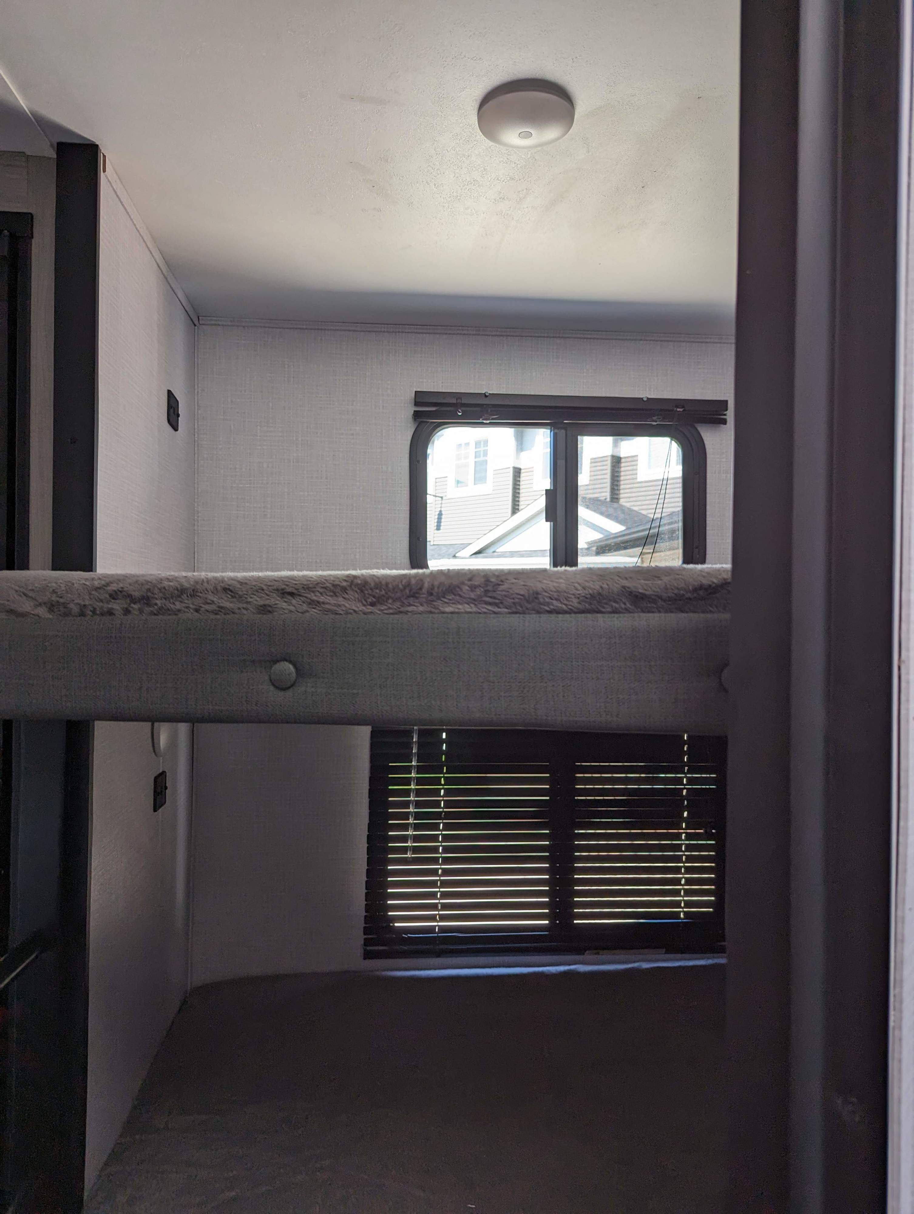 View from lower bunk in an RV rental, showing upper bunk, windows, & ceiling light.. Dutchmen Coleman Light 2022