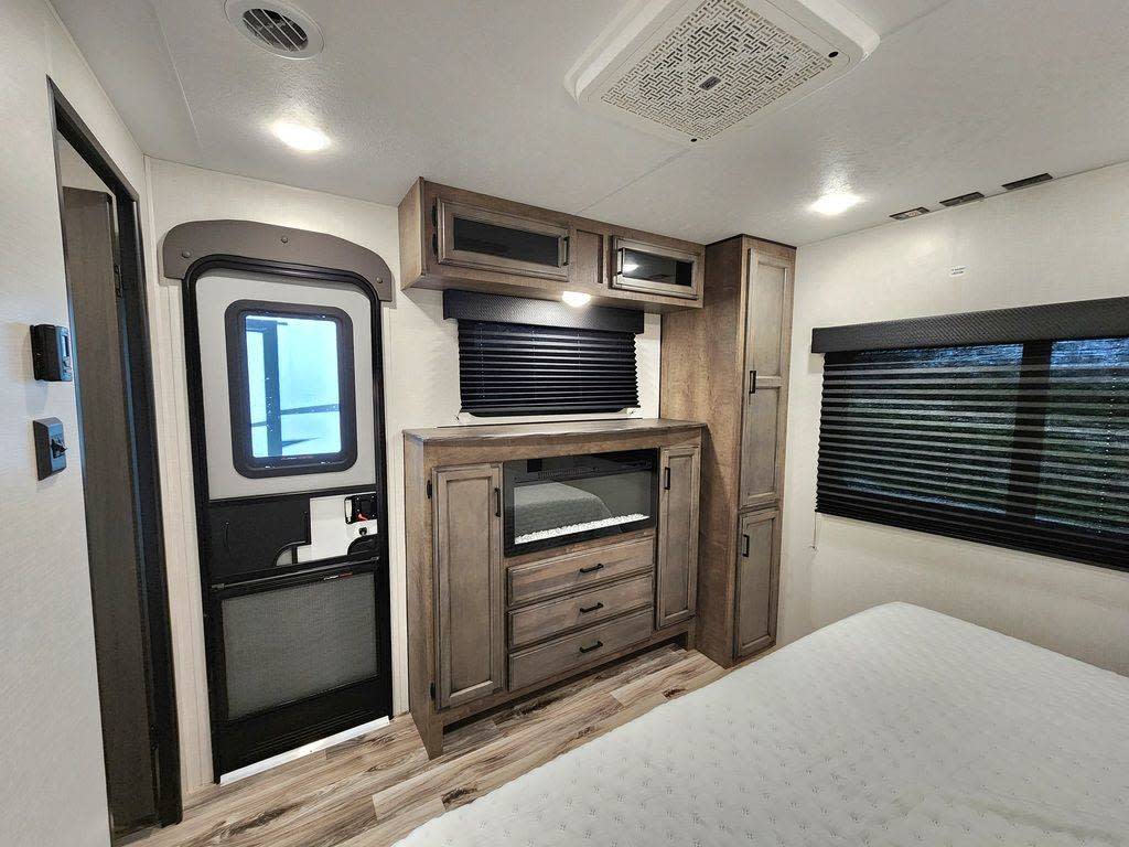 Inside an RV rental bedroom: features a cozy bed, window with blinds, storage unit with fireplace, and entry door. Perfect for travel.. SportTrek STT333VFK 2023