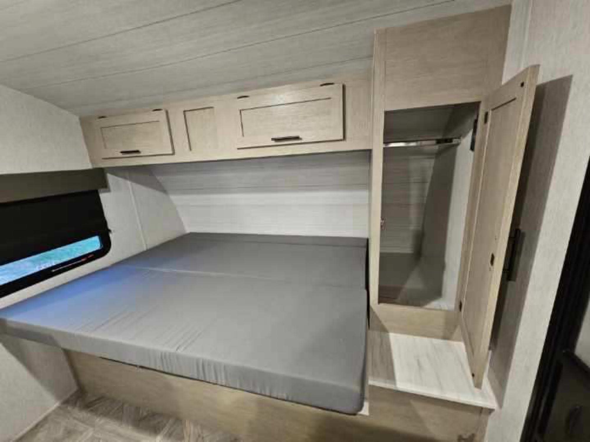 Cozy RV rental bedroom featuring a grey mattress, overhead light wood cabinets, and a tall wardrobe on the right.. Forest River Salem Cruise Lite 2024