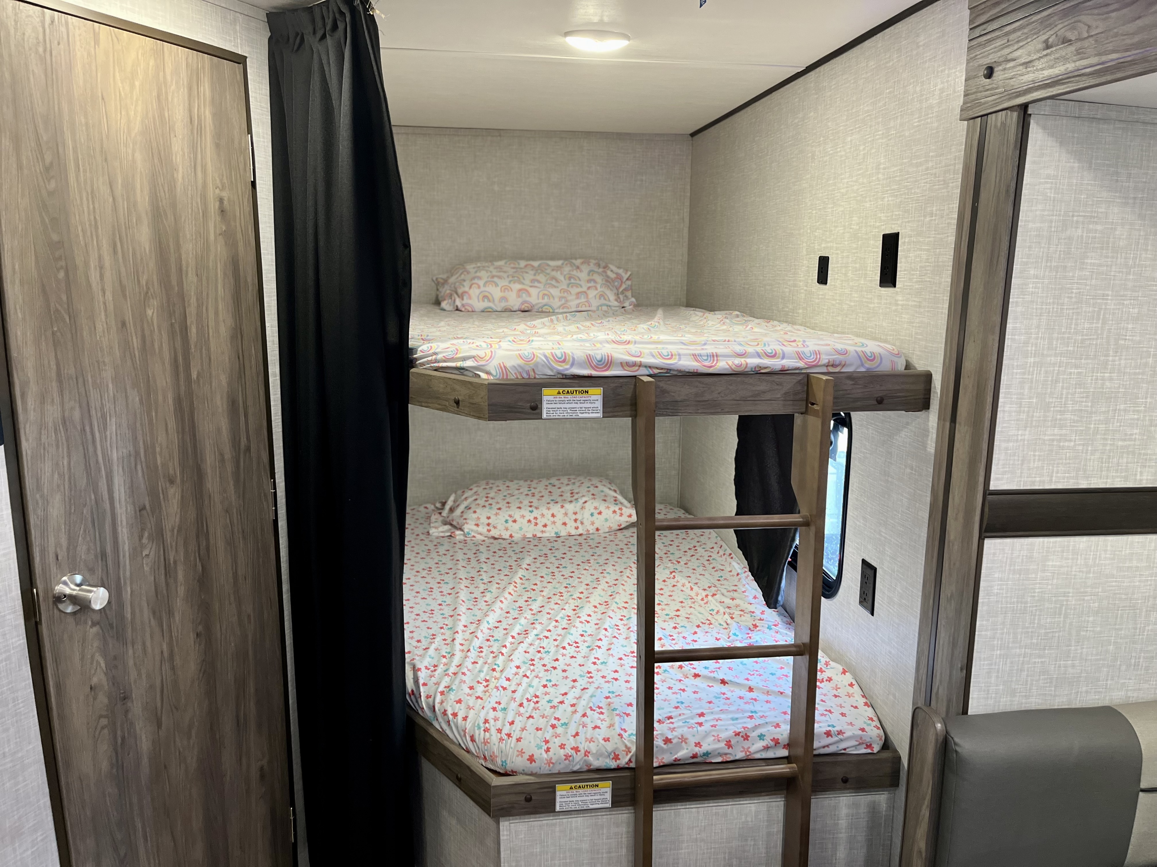RV rental interior featuring two bunk beds with colorful patterned sheets, a door, and privacy curtain.. Crossroads RV Zinger Lite 2022