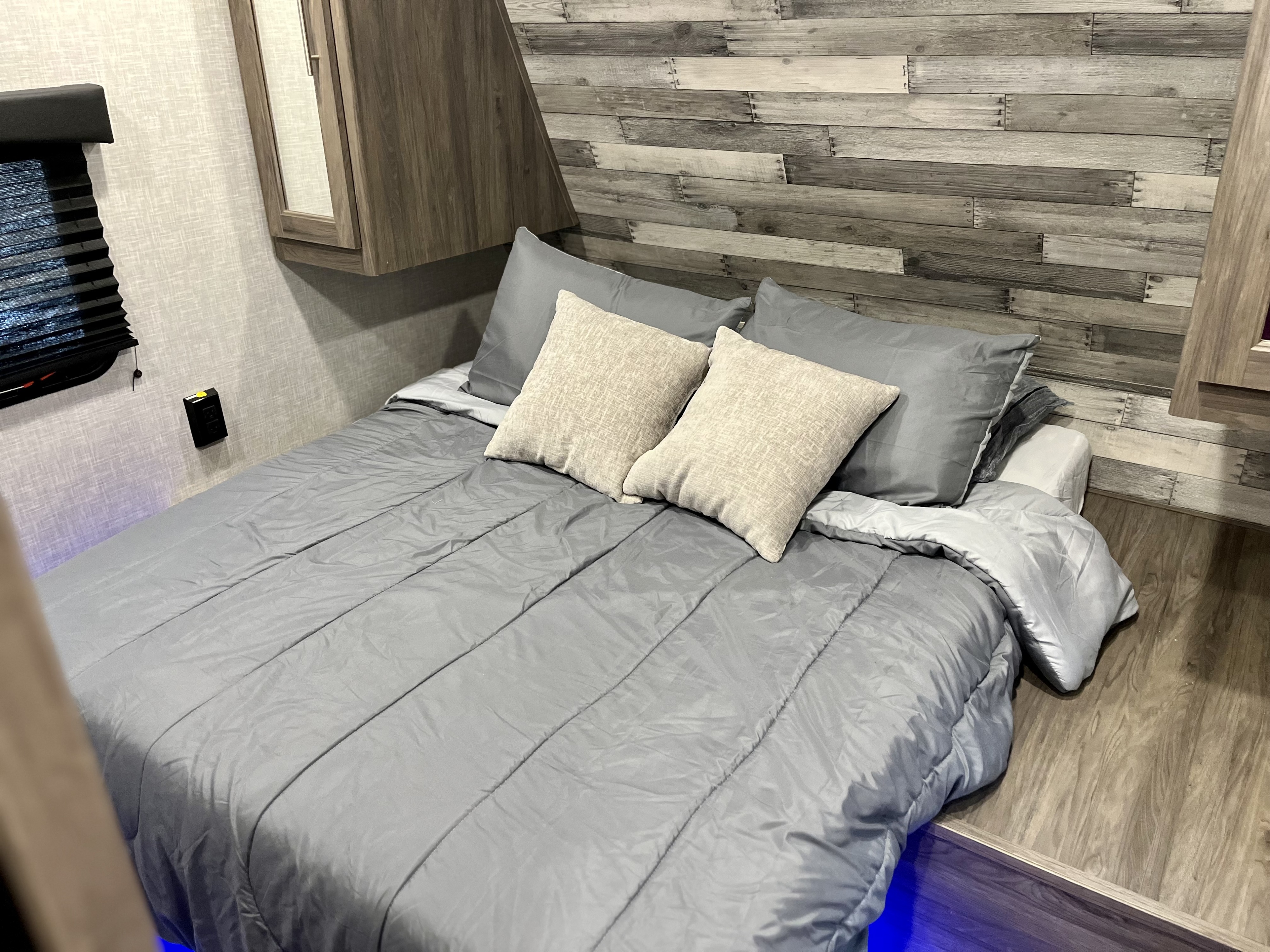 Cozy RV rental bedroom featuring a grey bed, comfy pillows, wood-look walls, and blue ambient lighting.. Crossroads RV Zinger Lite 2022