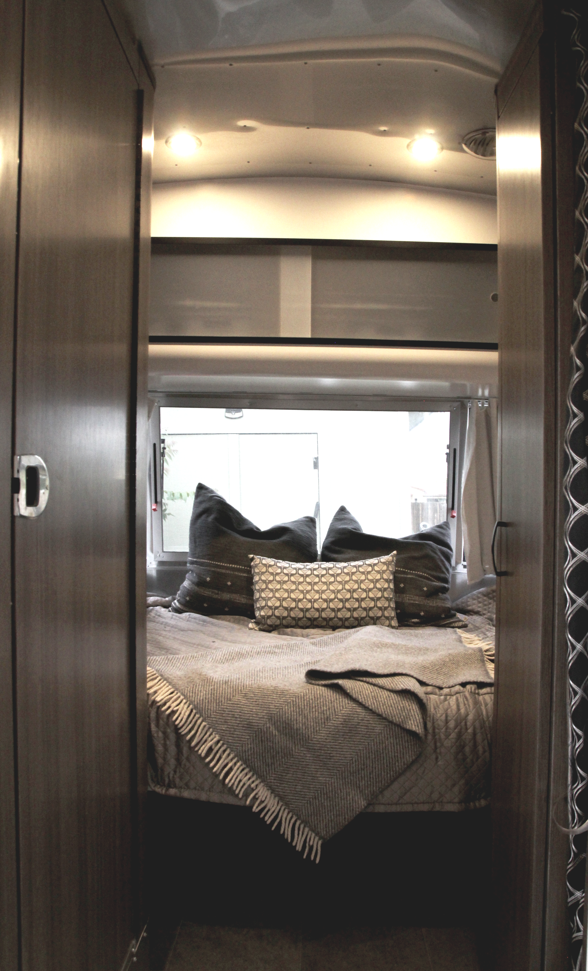 Inside an RV rental: a modern bedroom with a bed, patterned pillows, and a throw, seen from a warm wooden doorway.. Airstream Caravel 2022