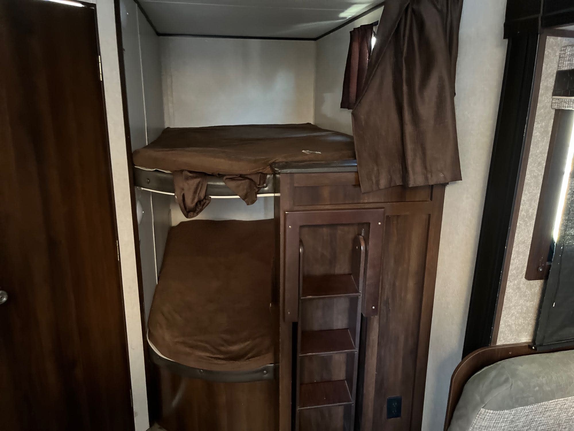 RV rental bunk beds with brown bedding. Features a wooden storage unit with shelves and a dark wooden door nearby.. Jayco Jay Flight 2018