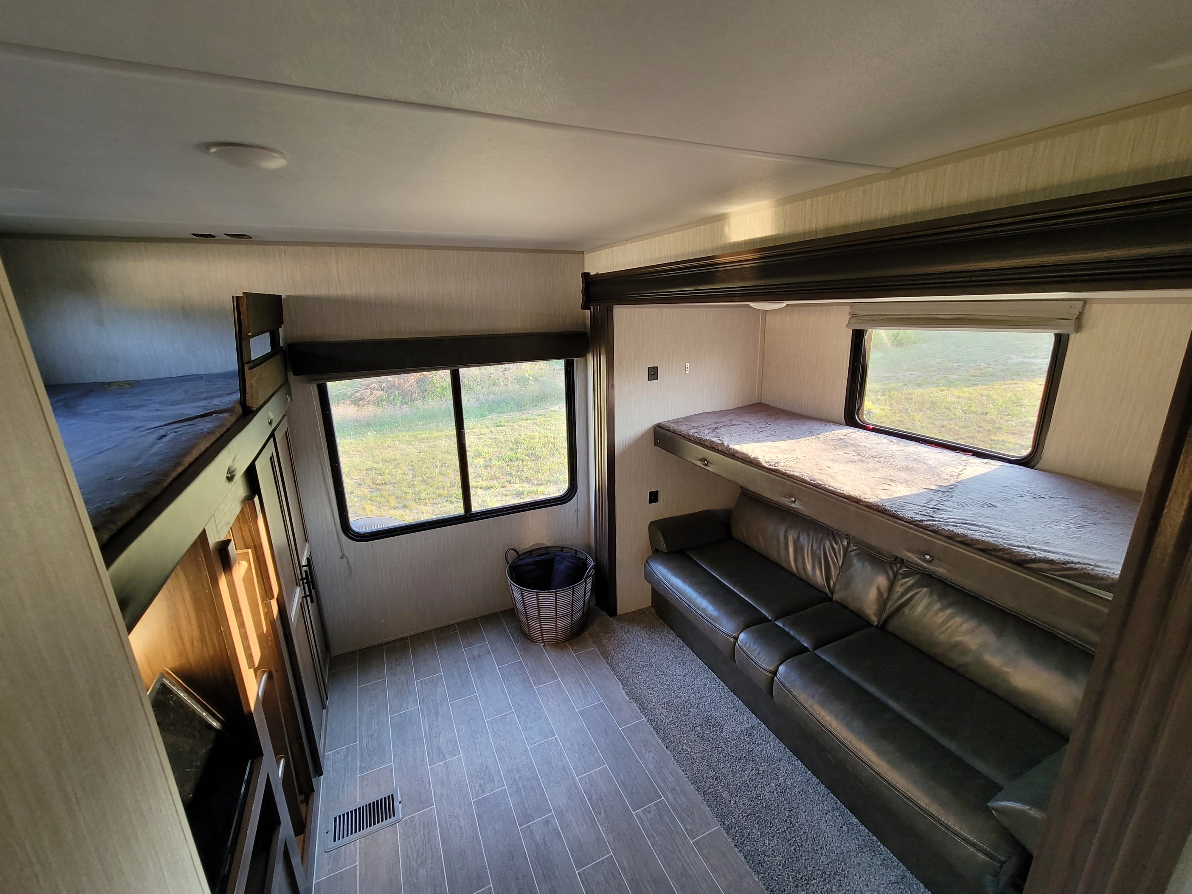 RV rental interior showing bunk beds, a dark sofa, and windows with outdoor views, offering comfortable lodging.. Forest River Cherokee 2020