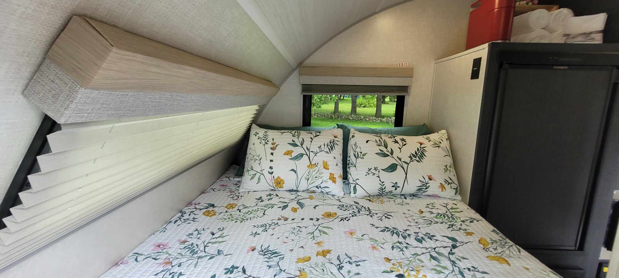 Cozy RV rental bedroom with floral bed, nature view from window, and compact fridge.. Forest River Other 2023