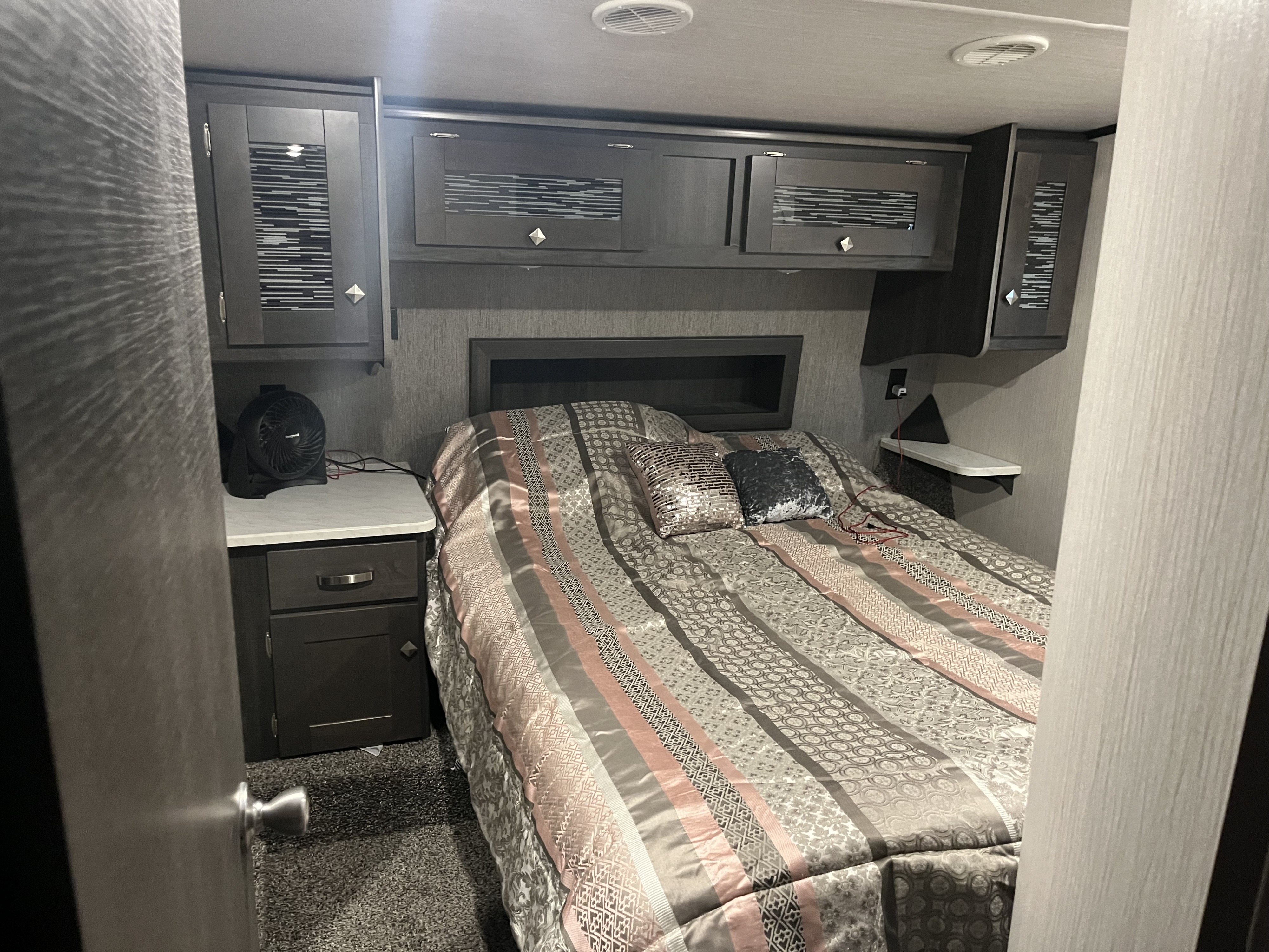 Cozy RV rental bedroom with a full bed, overhead storage cabinets, and nightstands, perfect for comfortable travel.. Heartland Fuel 335 2021