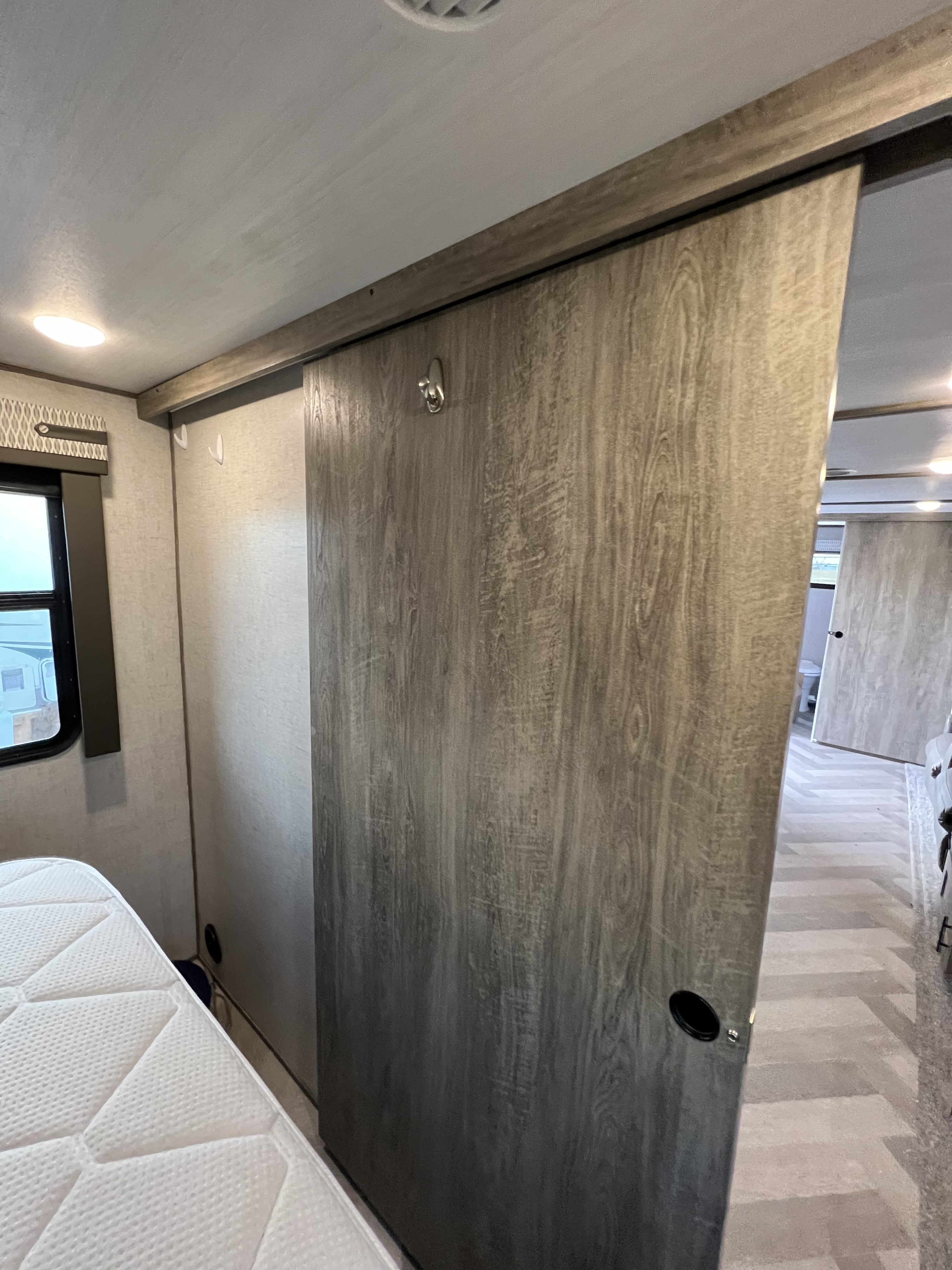 RV rental interior featuring a wood-grain sliding door, maximizing space in a compact bedroom with a white mattress.. Forest River Wildwood Heritage Glen HL 2021