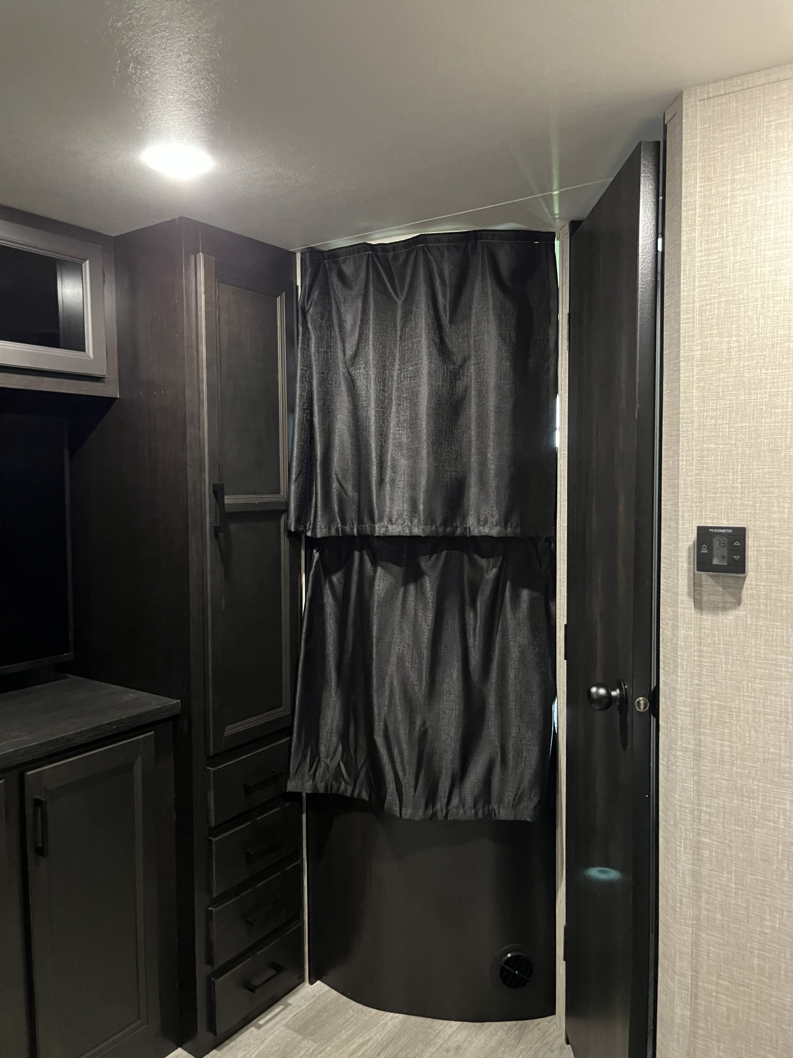 Compact RV rental interior featuring dark wood cabinets, TV, and a privacy curtain over a shower entrance. Functional RV living space.. Jayco Jay Flight 2023