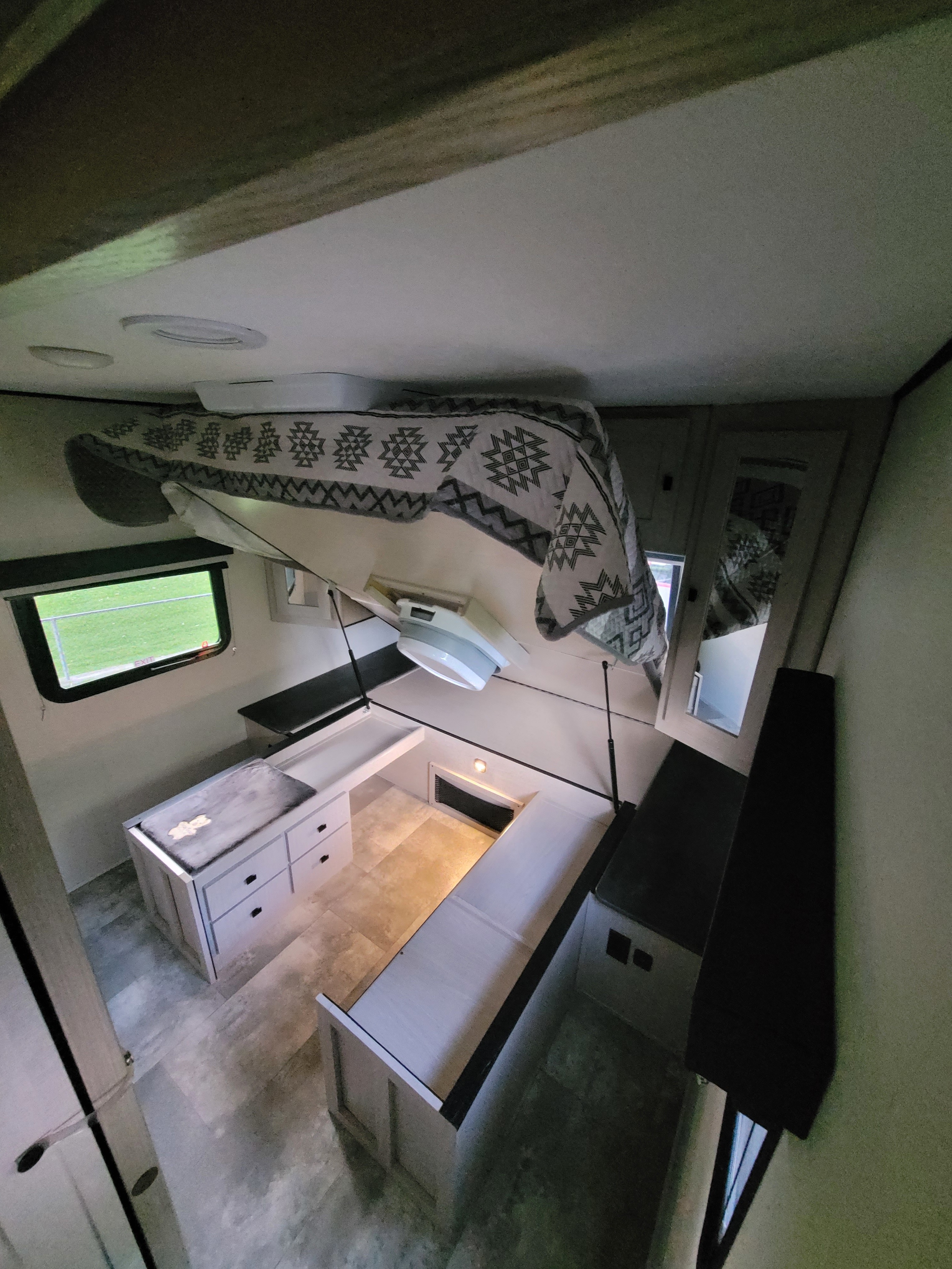 Compact RV rental interior showing a lifted bed over a versatile dinette and seating area with storage.. Coachmen Apex 2023